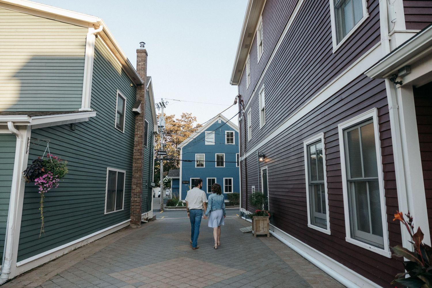 Two people walk down a path between traditional New England style houses.