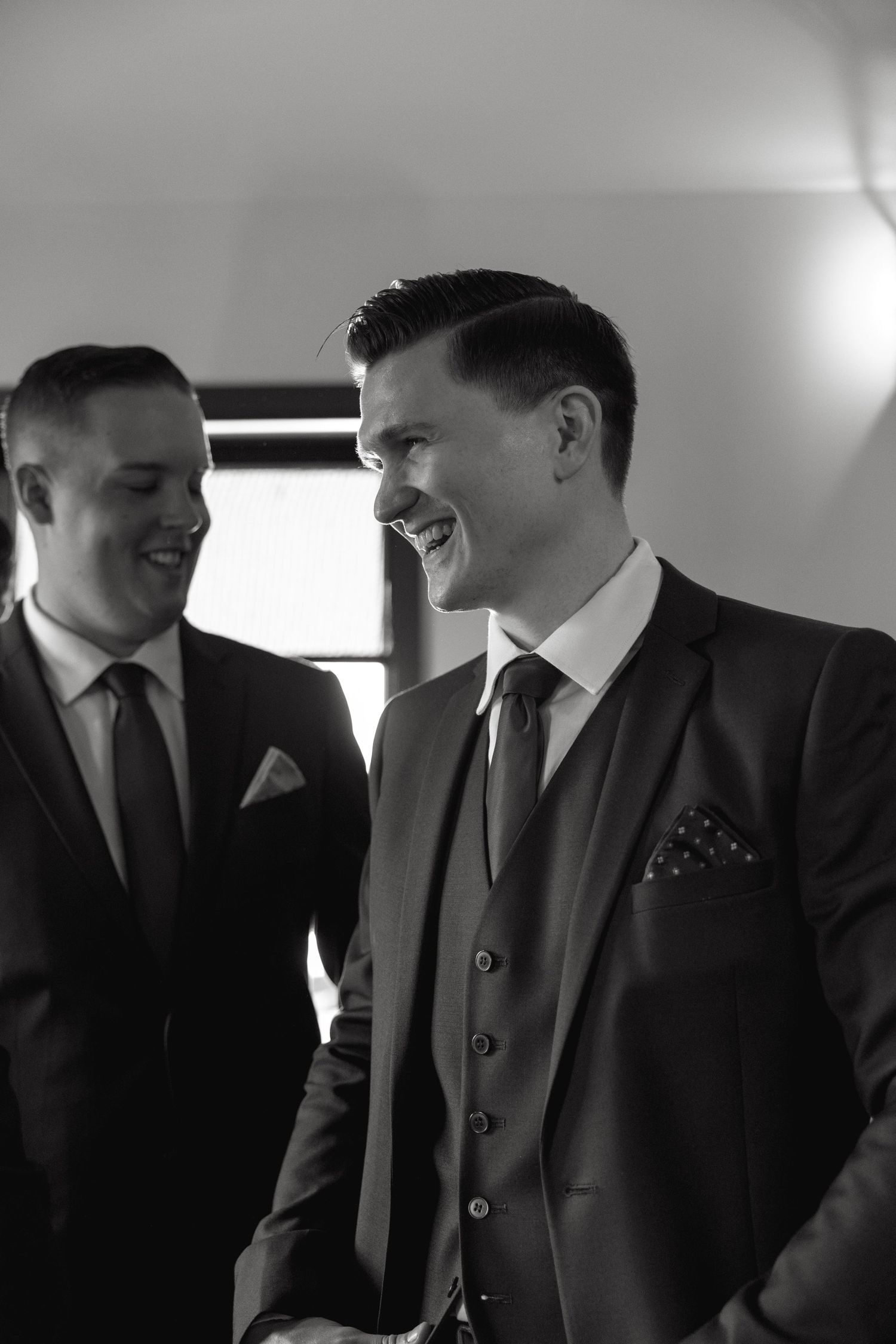 Groomsmen share a lighthearted moment while dressed in formal suits.