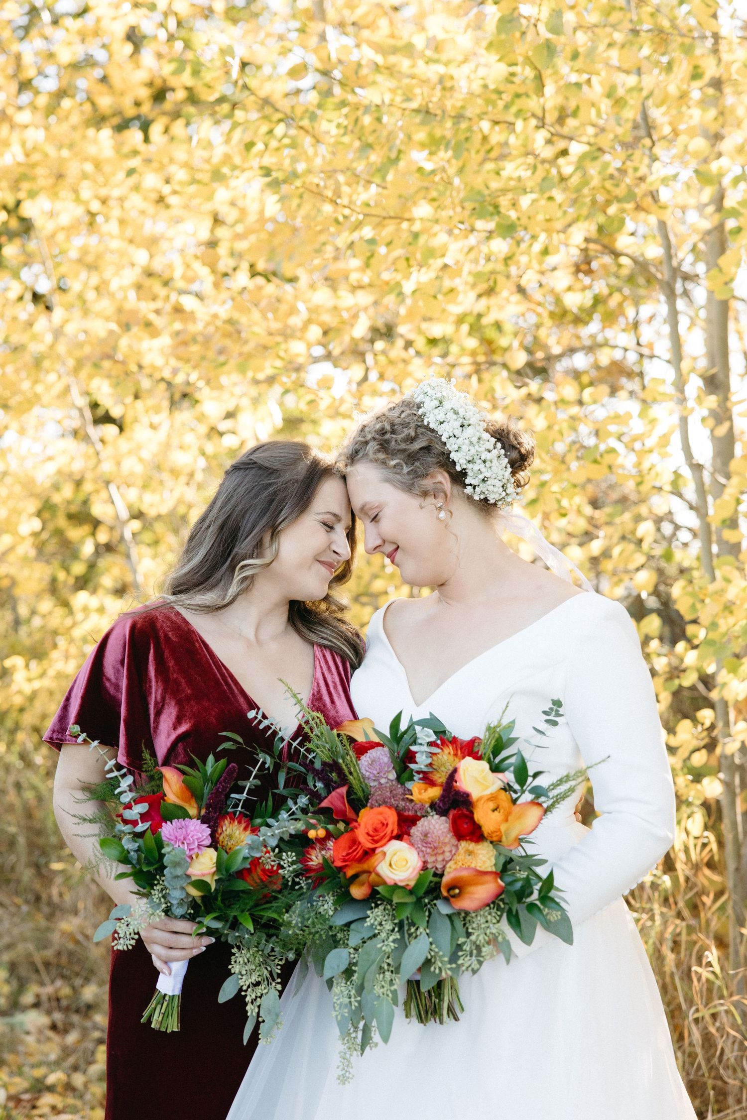 Intimate wedding portrait with colorful autumn bouquets against golden leaves.