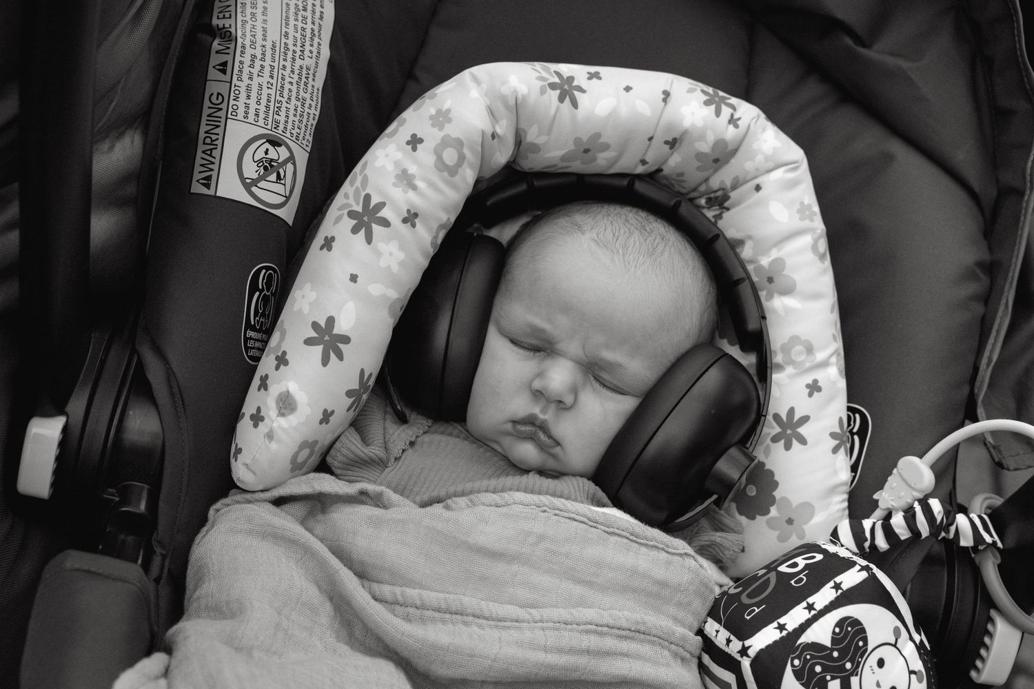 A sleeping baby wearing large headphones in a car seat with a star-patterned cushion.