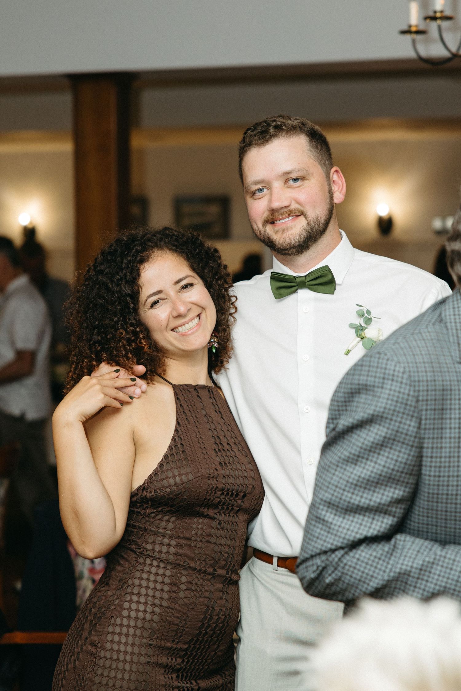 Smiling couple poses at wedding reception, man wearing green bow tie and white shirt with boutonniere.