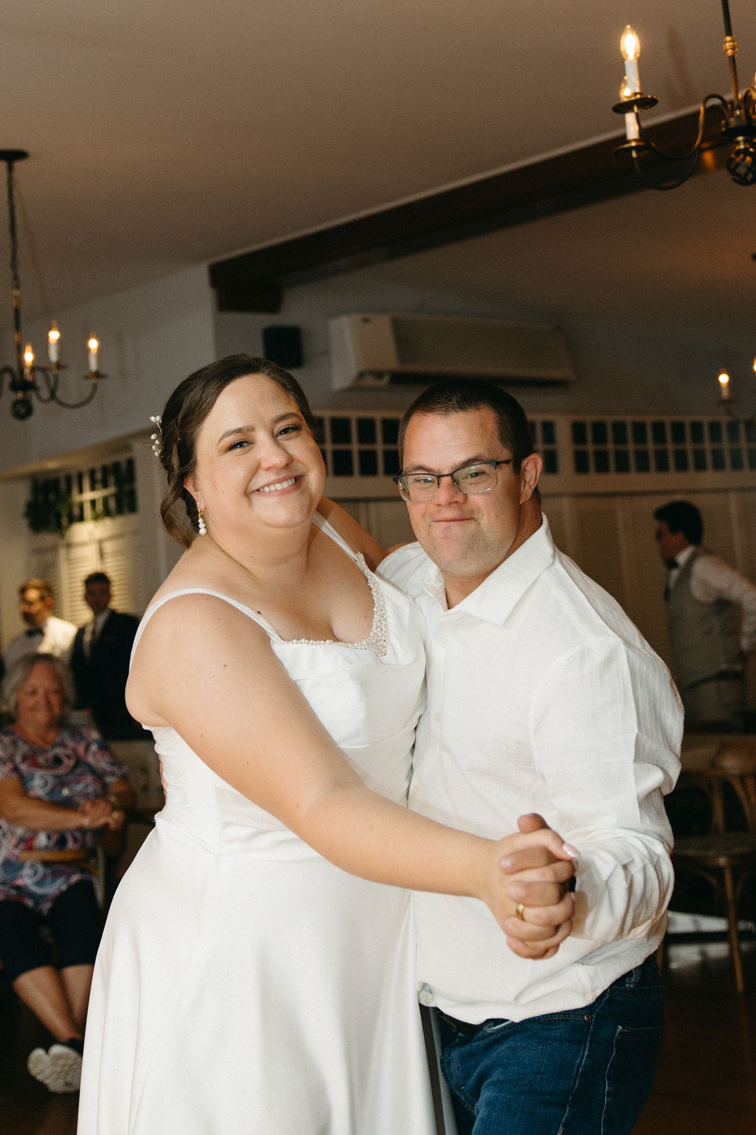 Bride and groom sharing their first dance, smiling at camera in a warmly lit wedding reception venue.