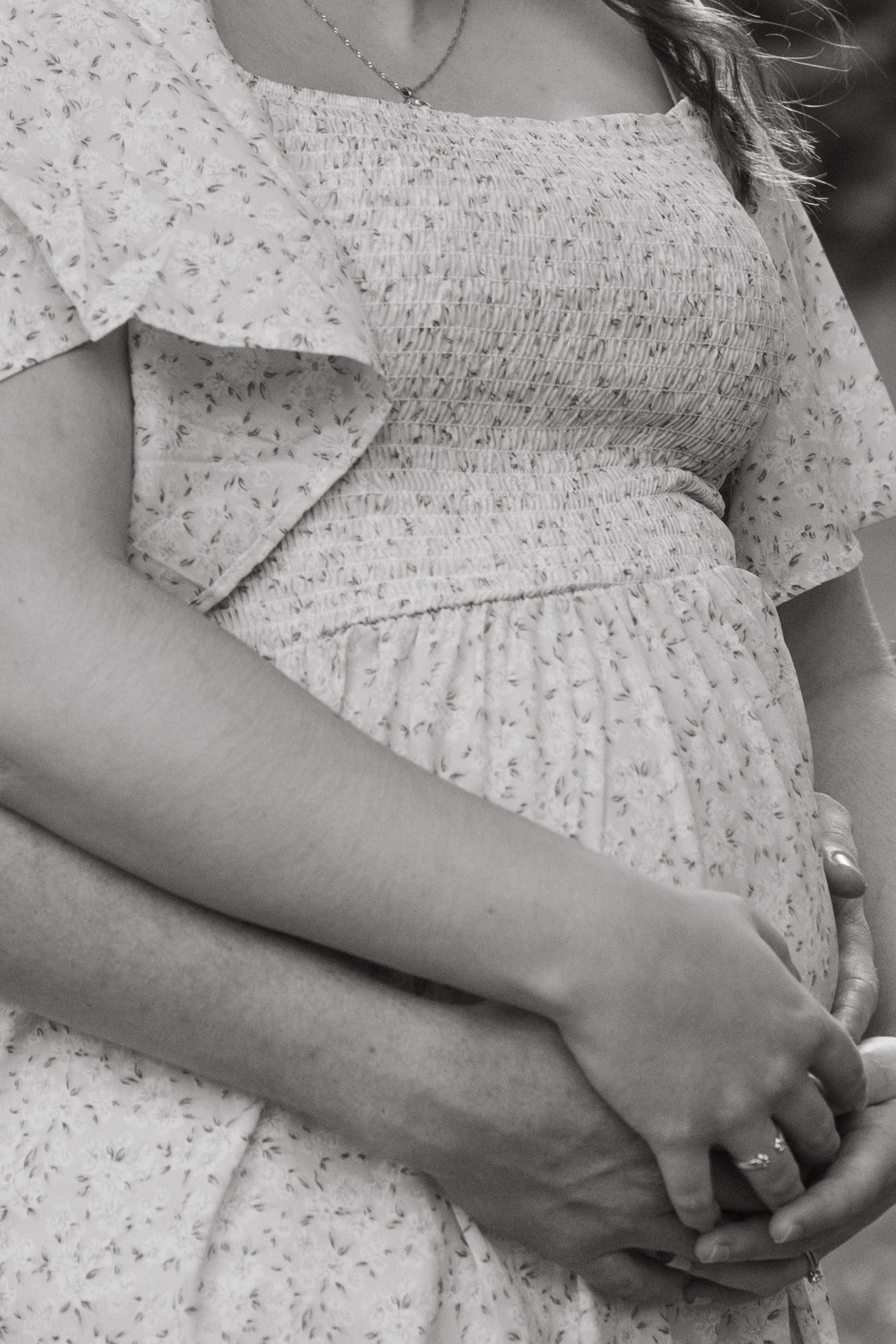 Close-up black and white detail shots of hands resting on a floral patterned dress.