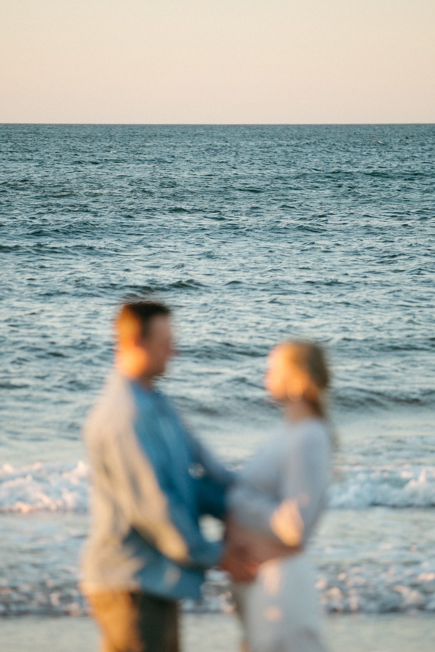 Silhouetted couple standing together by the ocean at sunset.