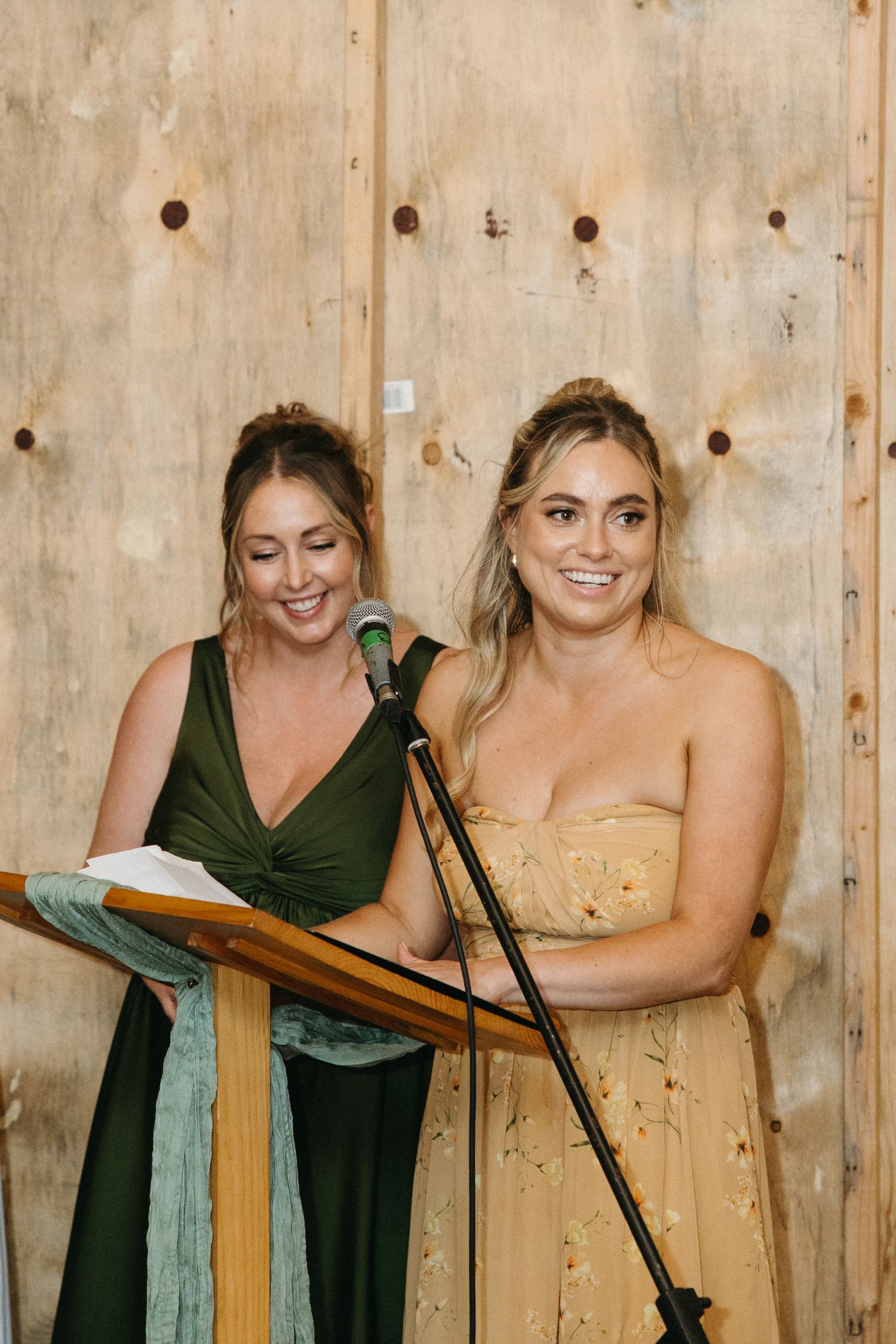 Wedding party members lean on wooden podiums while sharing laughs together.