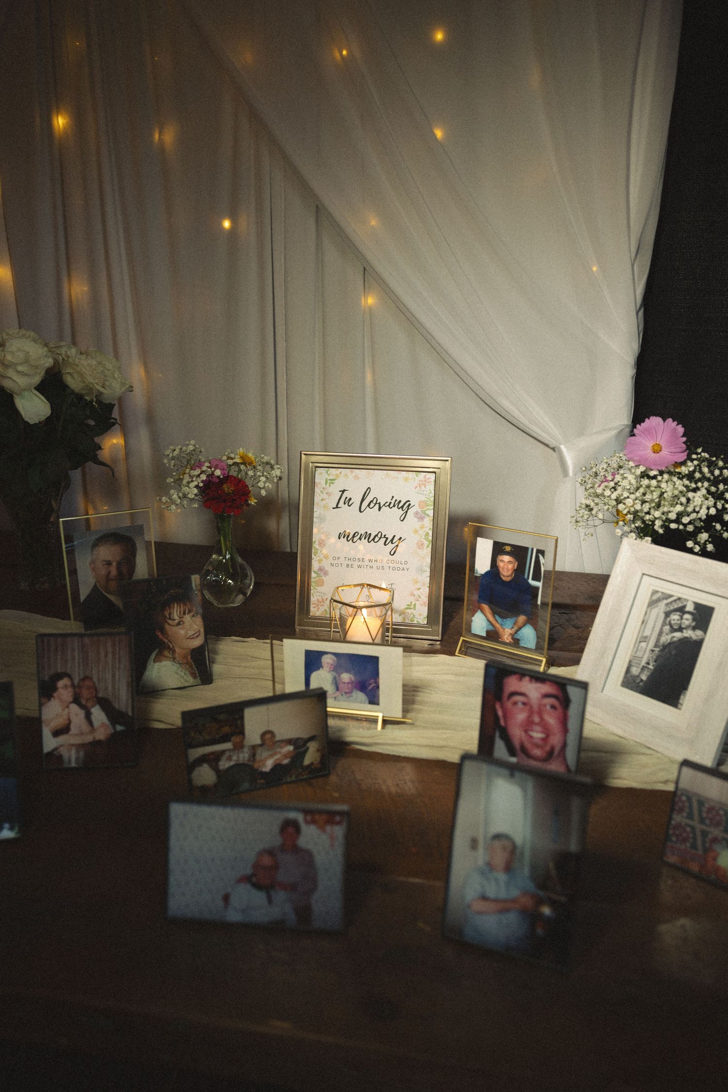 A memorial display with framed photos, flowers, and candles under soft lighting.