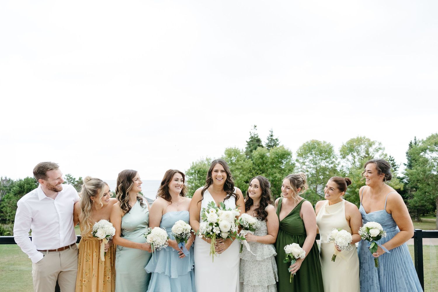 Wedding party in mixed pastel and jewel-toned dresses posing together outdoors.