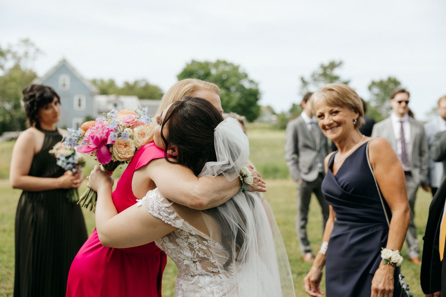 Wedding party members embrace and celebrate during an outdoor reception.