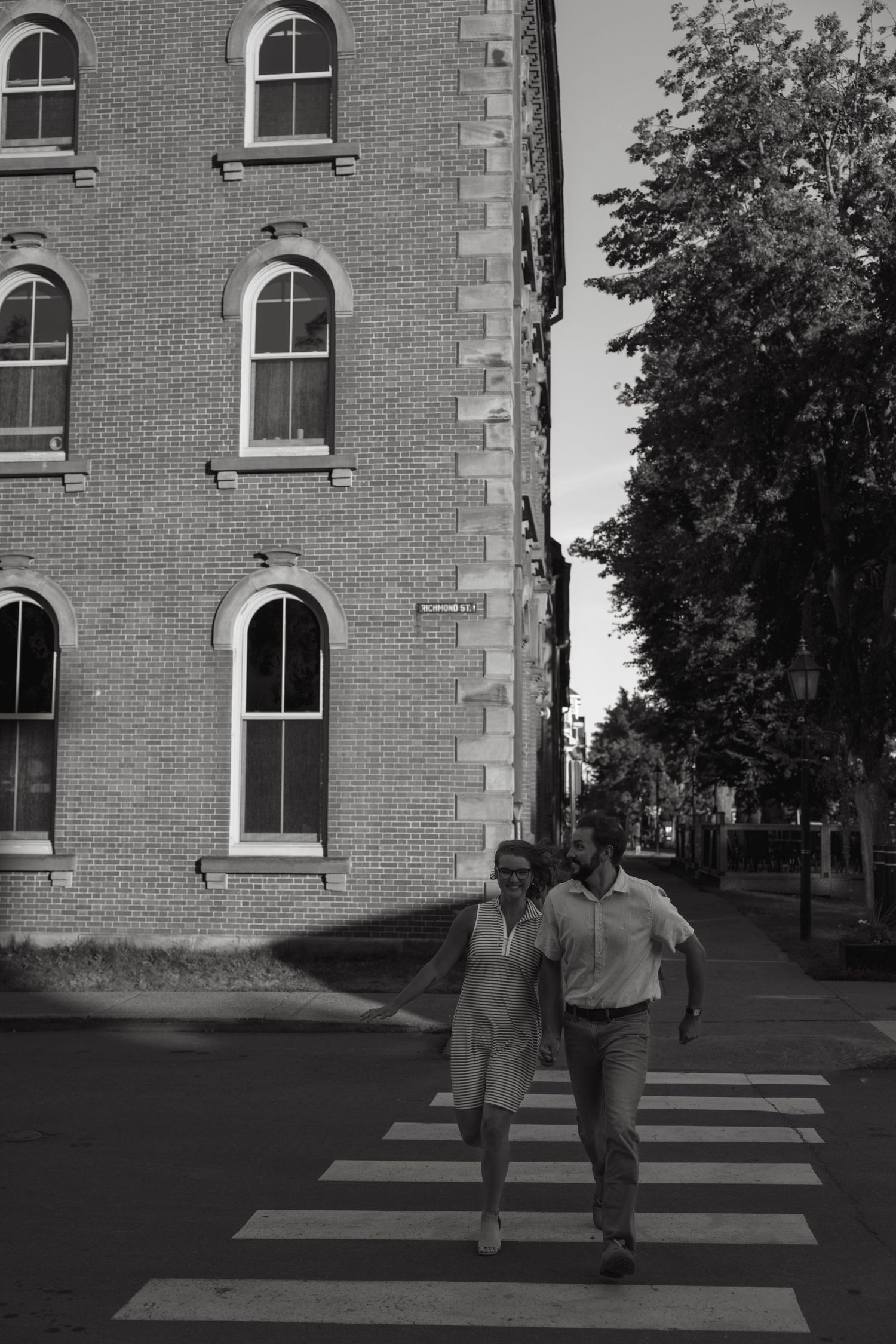 Two people walk across a crosswalk near a brick building in black and white.