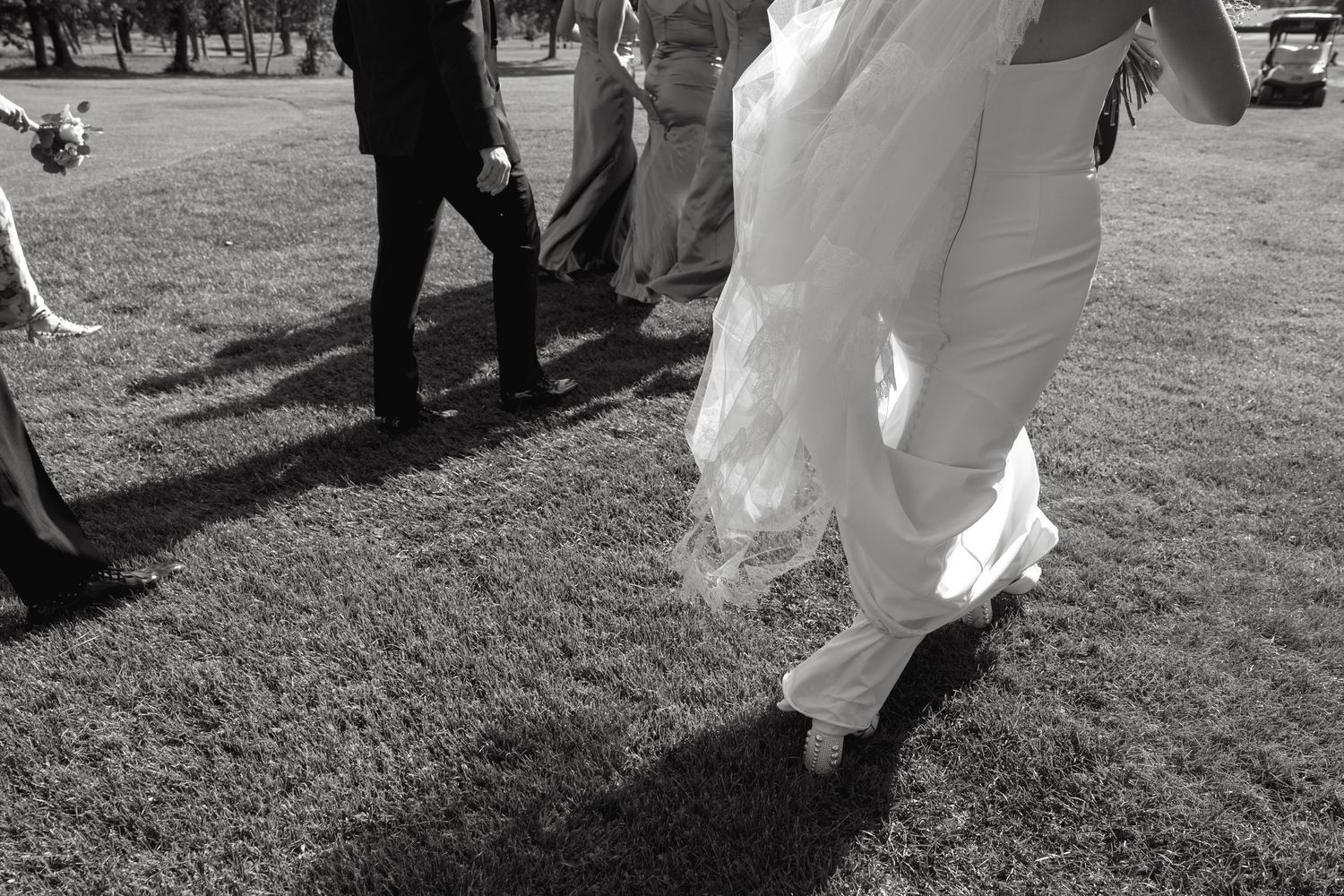 Wedding party members walk across a grassy lawn in black and white.