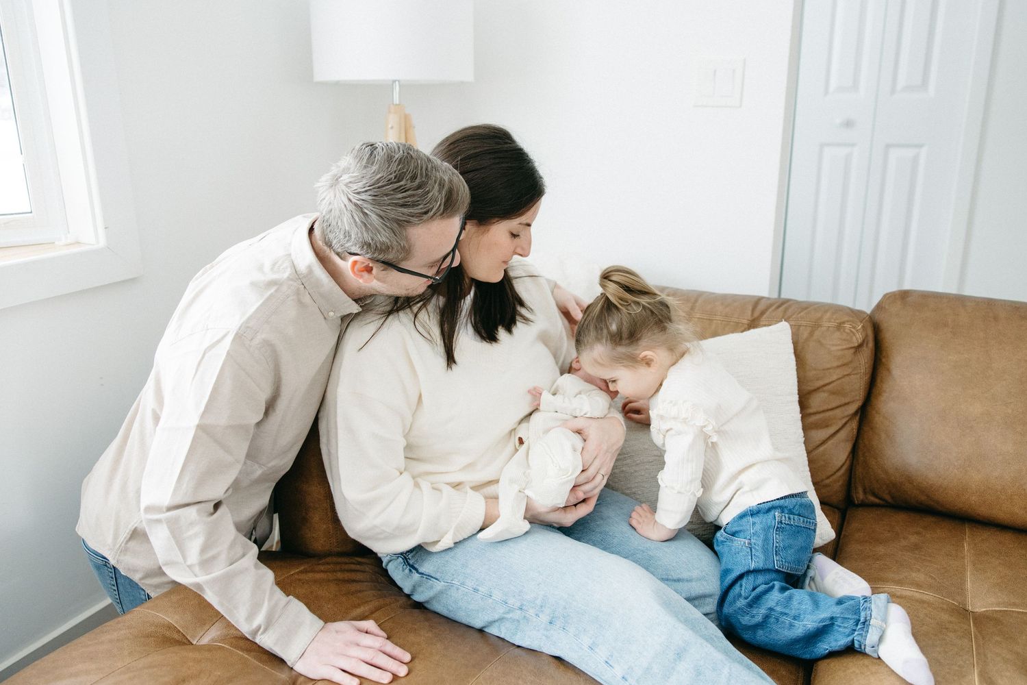 Family relaxing together on brown leather couch in casual white and denim outfits.