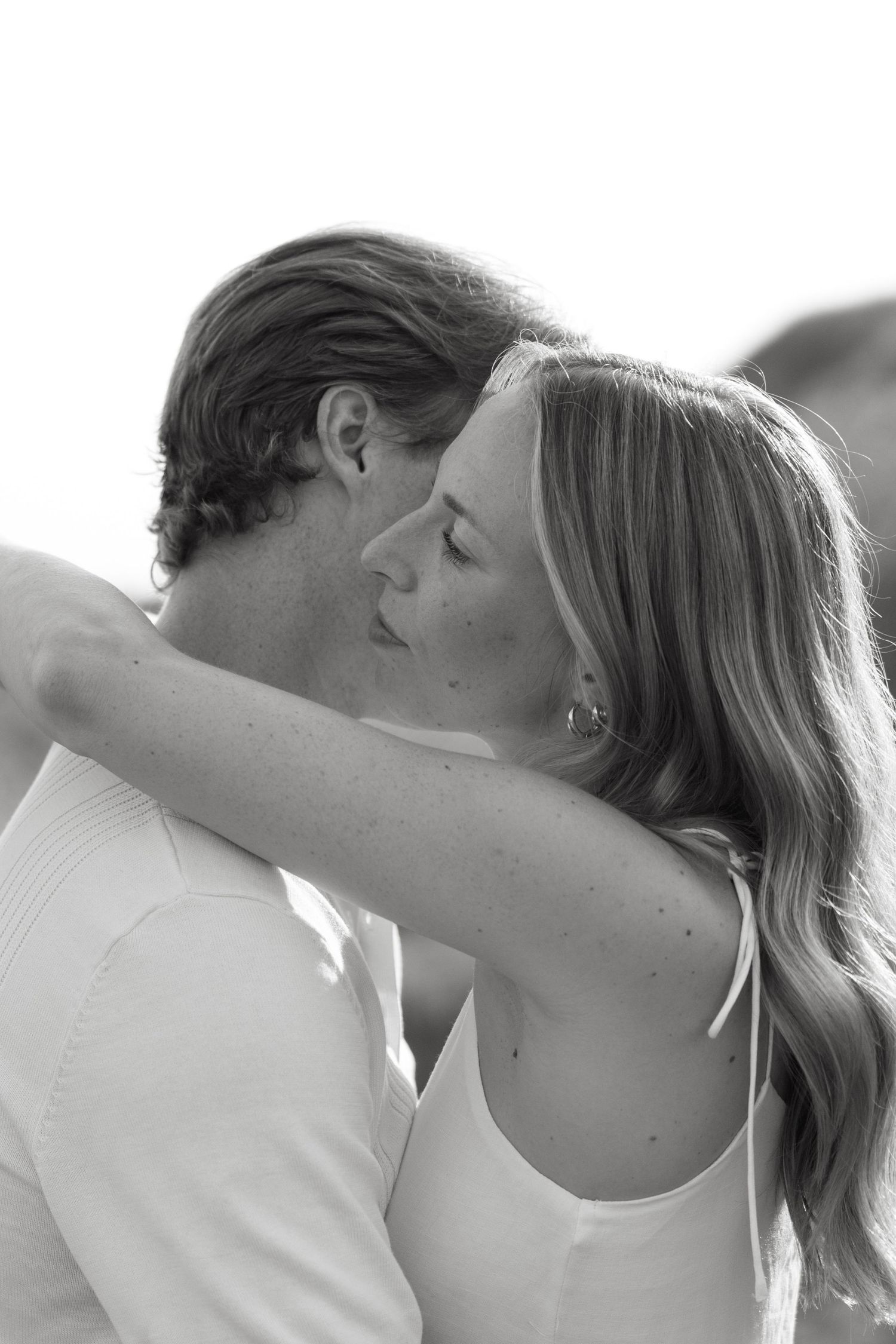 Black and white photo of couple about to kiss, woman with long hair embracing man outdoors.