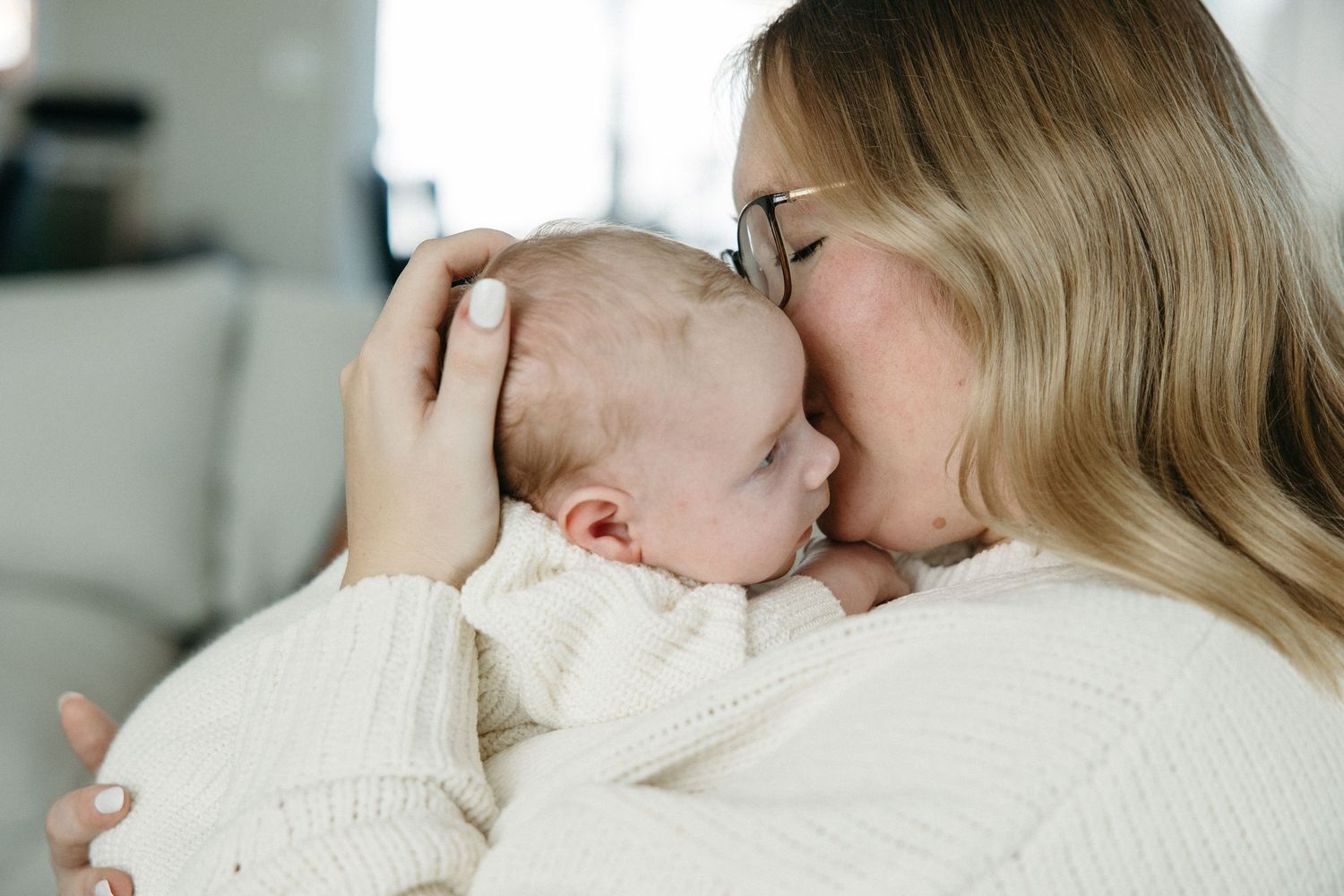 Parents in casual attire tenderly embrace their sleeping infant in a soft, natural light setting.