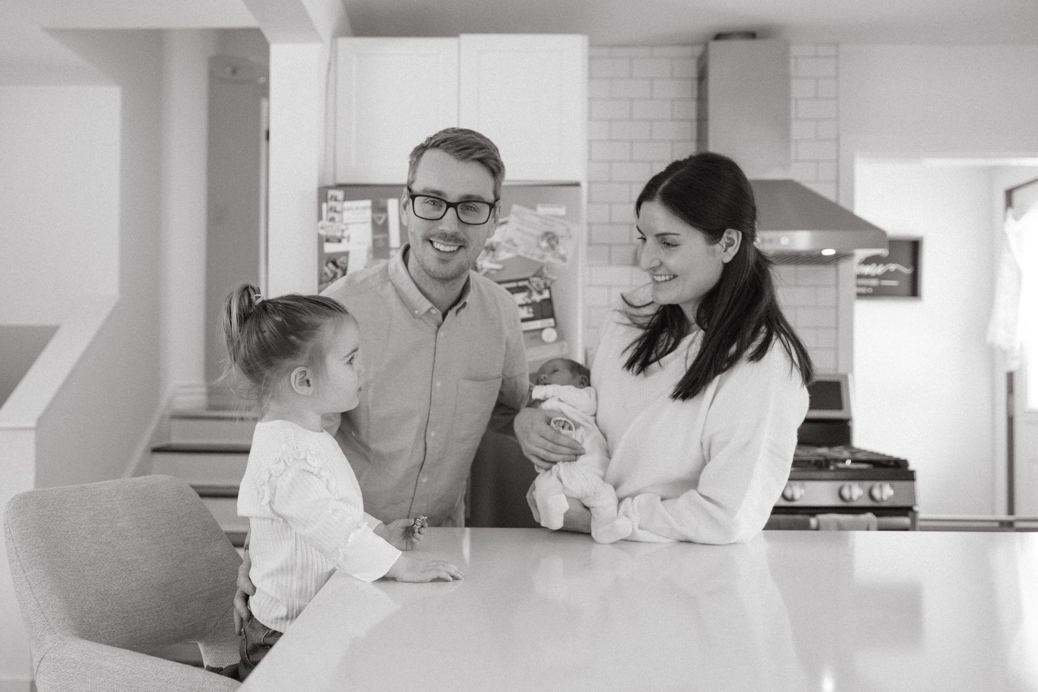 Family gathering in bright modern kitchen with white cabinets and natural lighting.