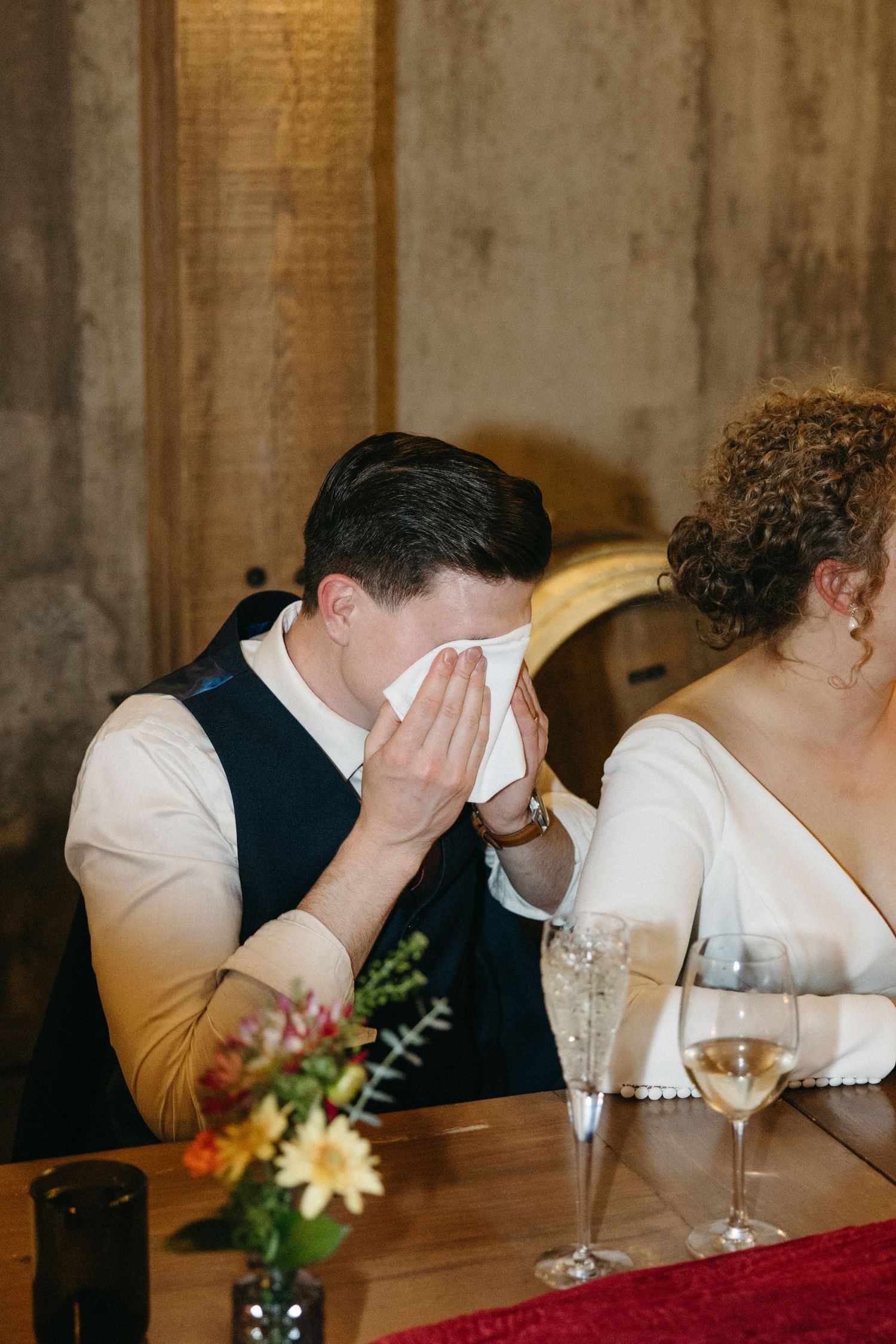 Wedding party members seated at head table wiping tears during emotional speeches.