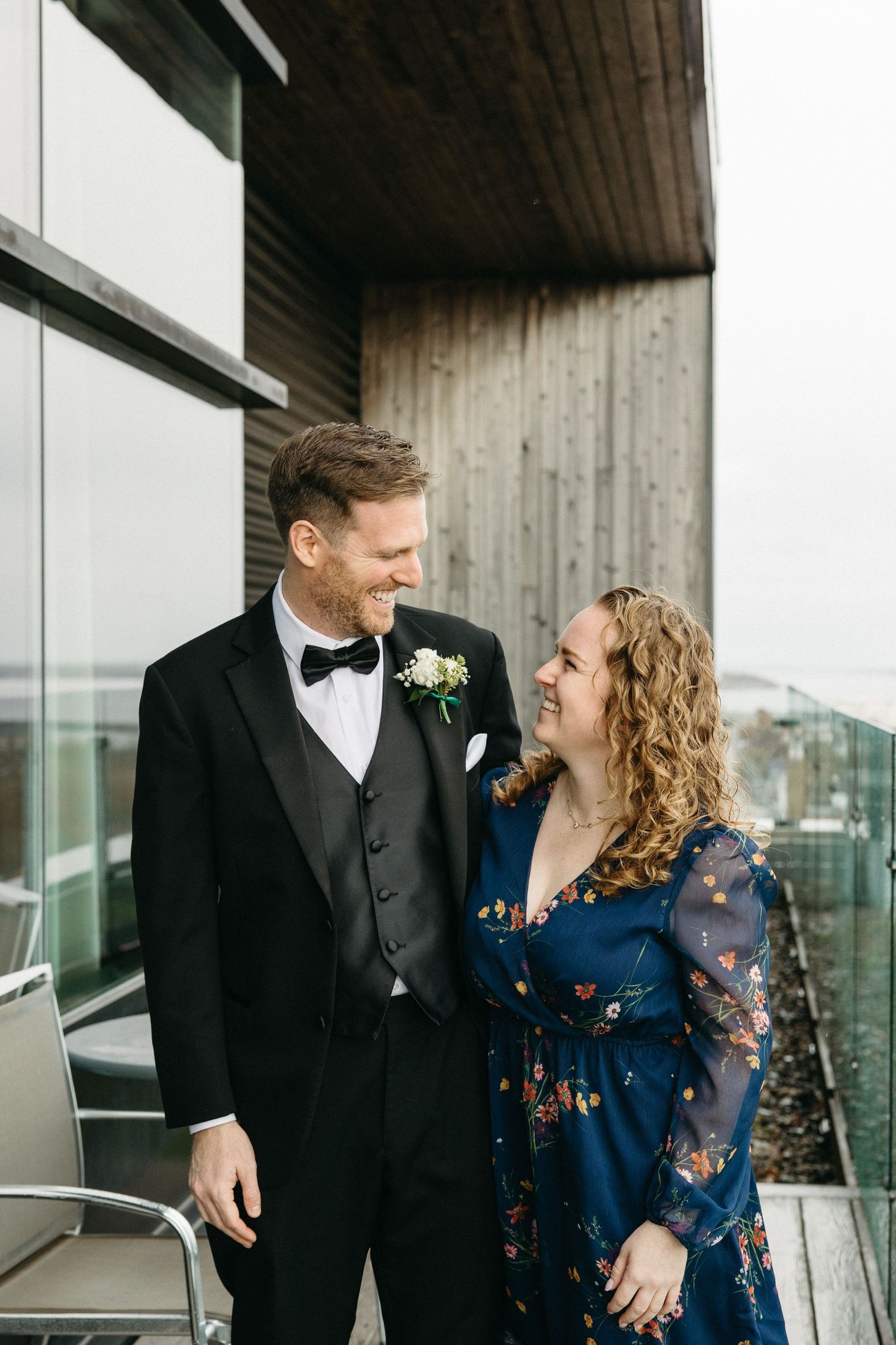 A couple shares a candid moment together on a modern balcony with glass railings.
