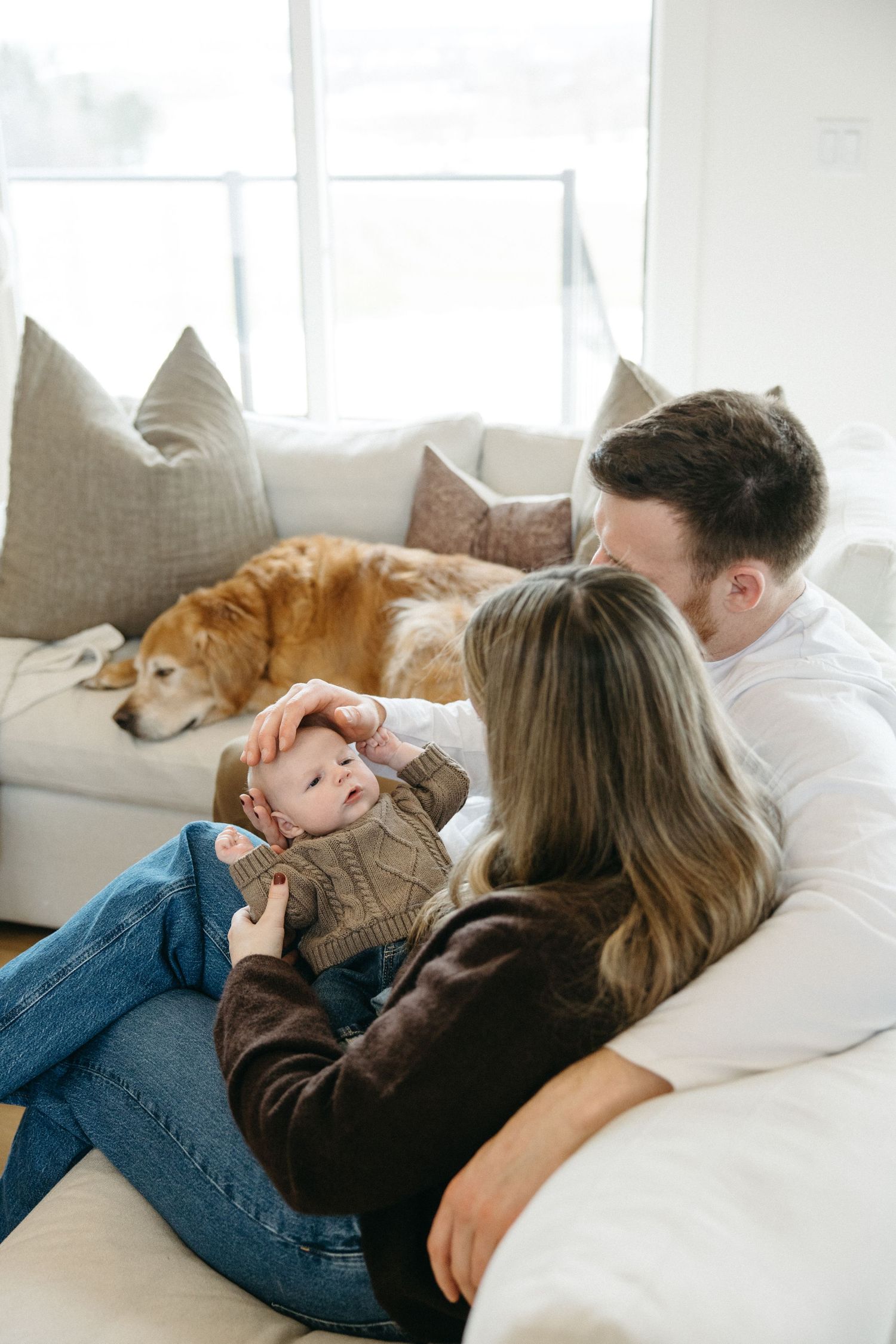 Family lounging on white couch with golden retriever visible in background.