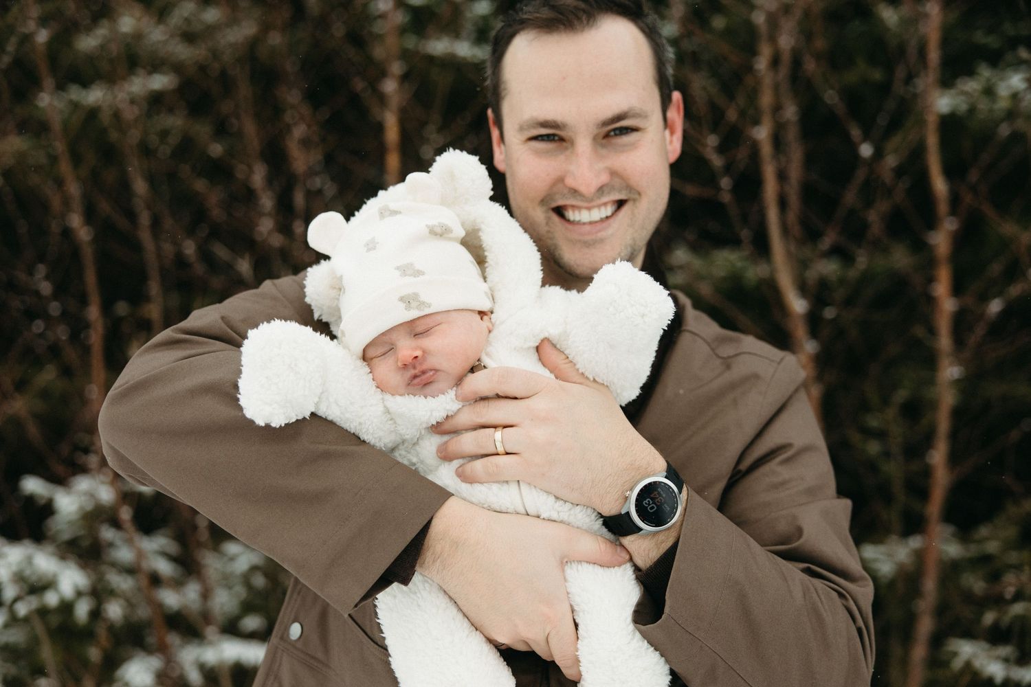 Winter family moment captured in snow with baby in plush white outfit.