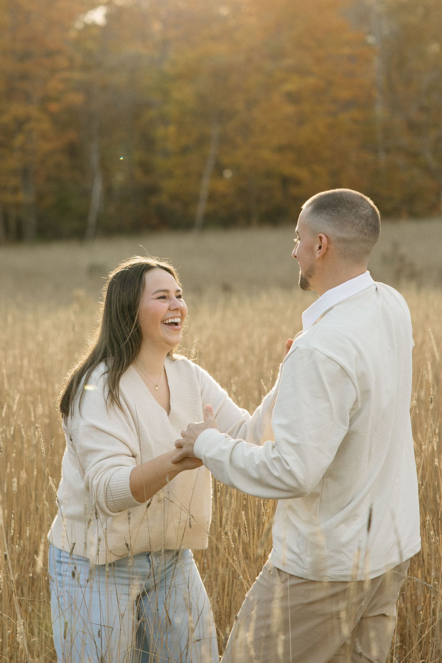 Two people in white clothing dance playfully in a golden wheat field.