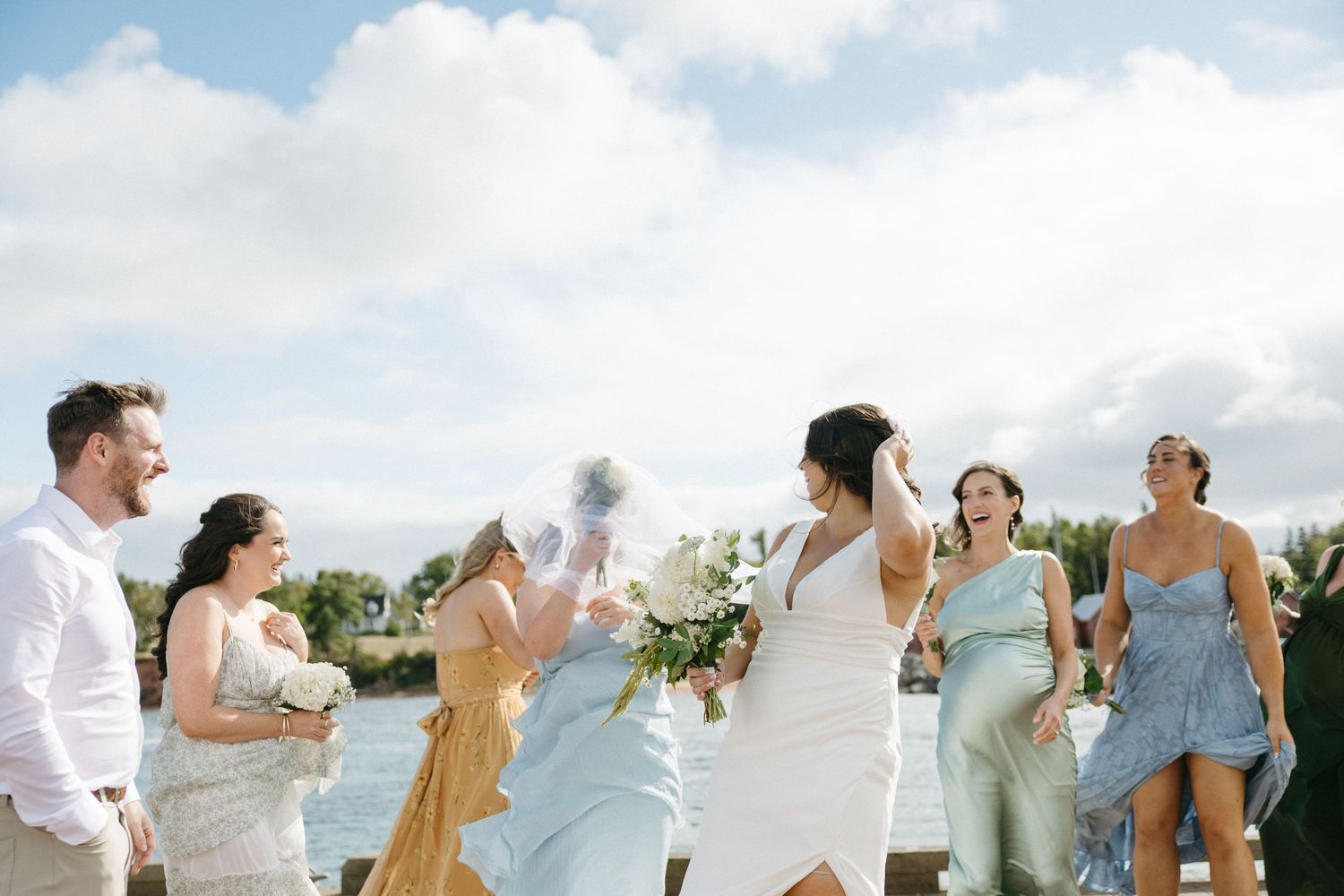 Wedding party celebrates joyfully outdoors under a bright blue sky.
