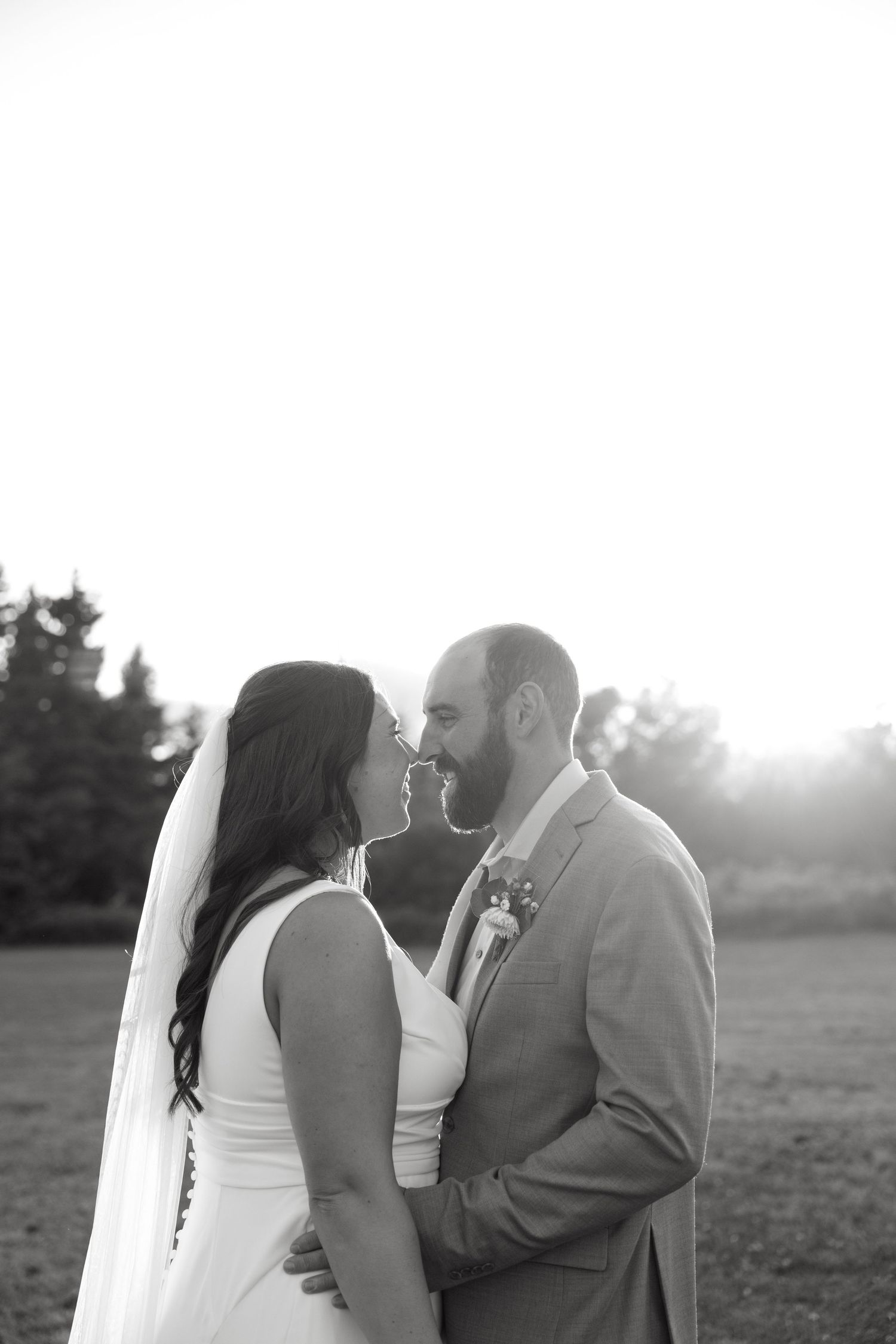 A romantic sunset photoshoot of a couple in formal attire standing in an open field.