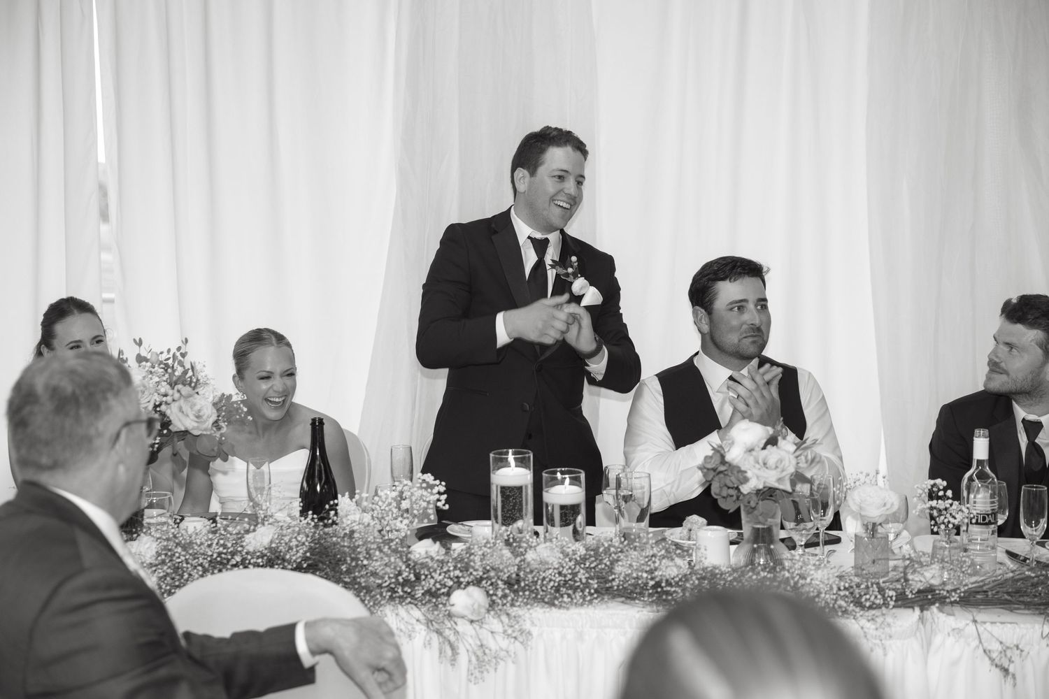 Black and white photo of wedding party during reception toasts and speeches.