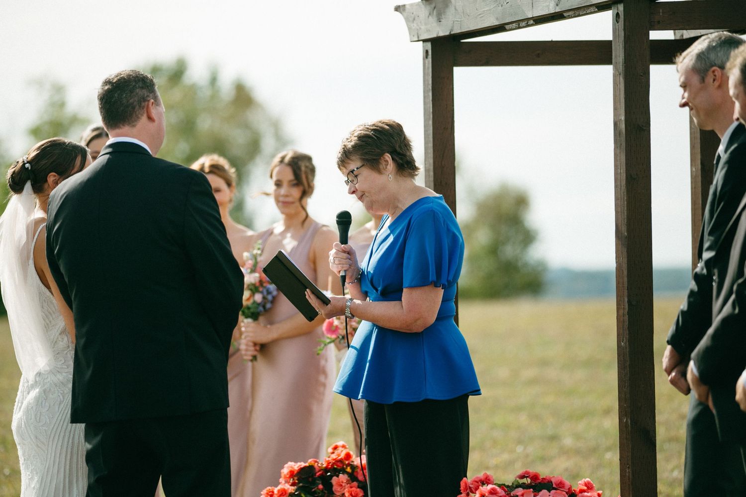 Wedding ceremony guests mingling under a wooden pergola structure.