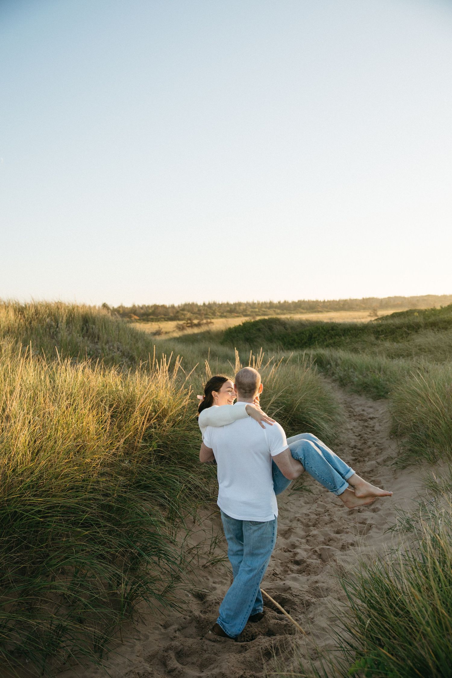 Couple walking and sitting together on sandy path through coastal grass.