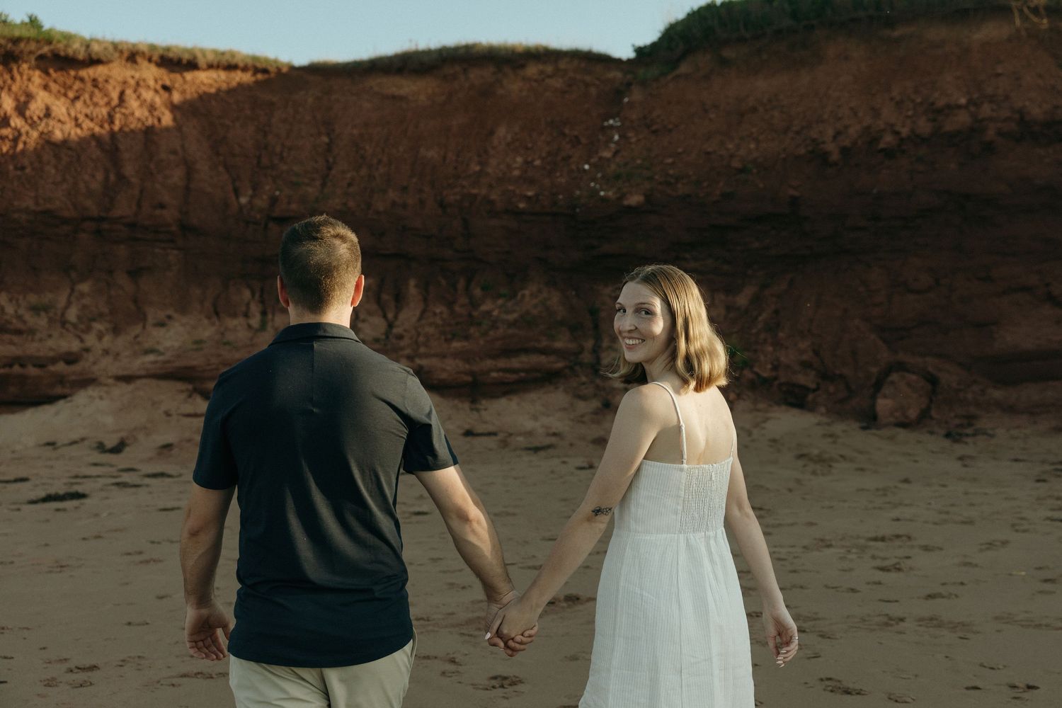 Silhouetted couple walking along beach cliffs during golden hour.