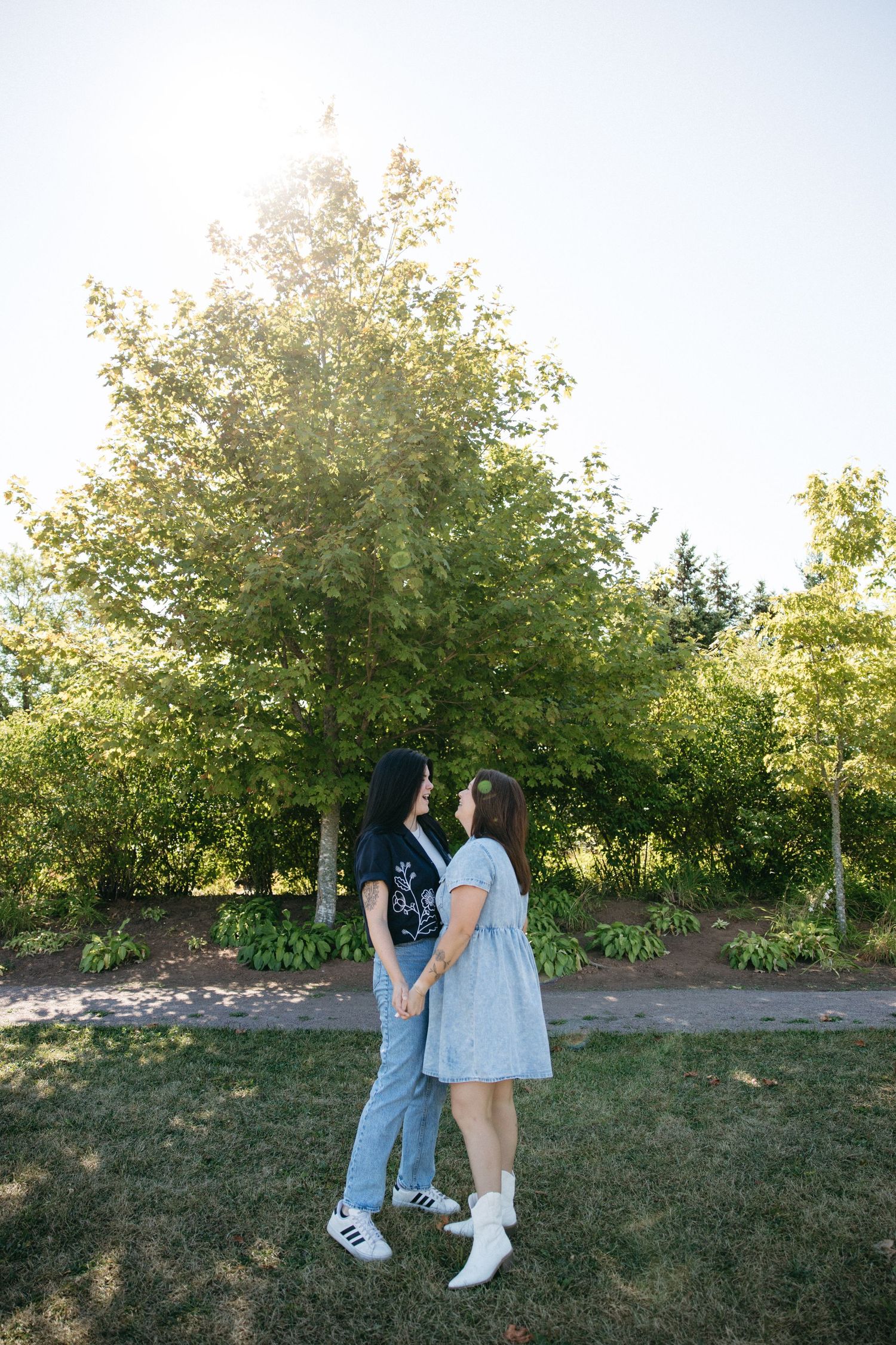 A couple standing together on grass with green trees in the background during golden hour.