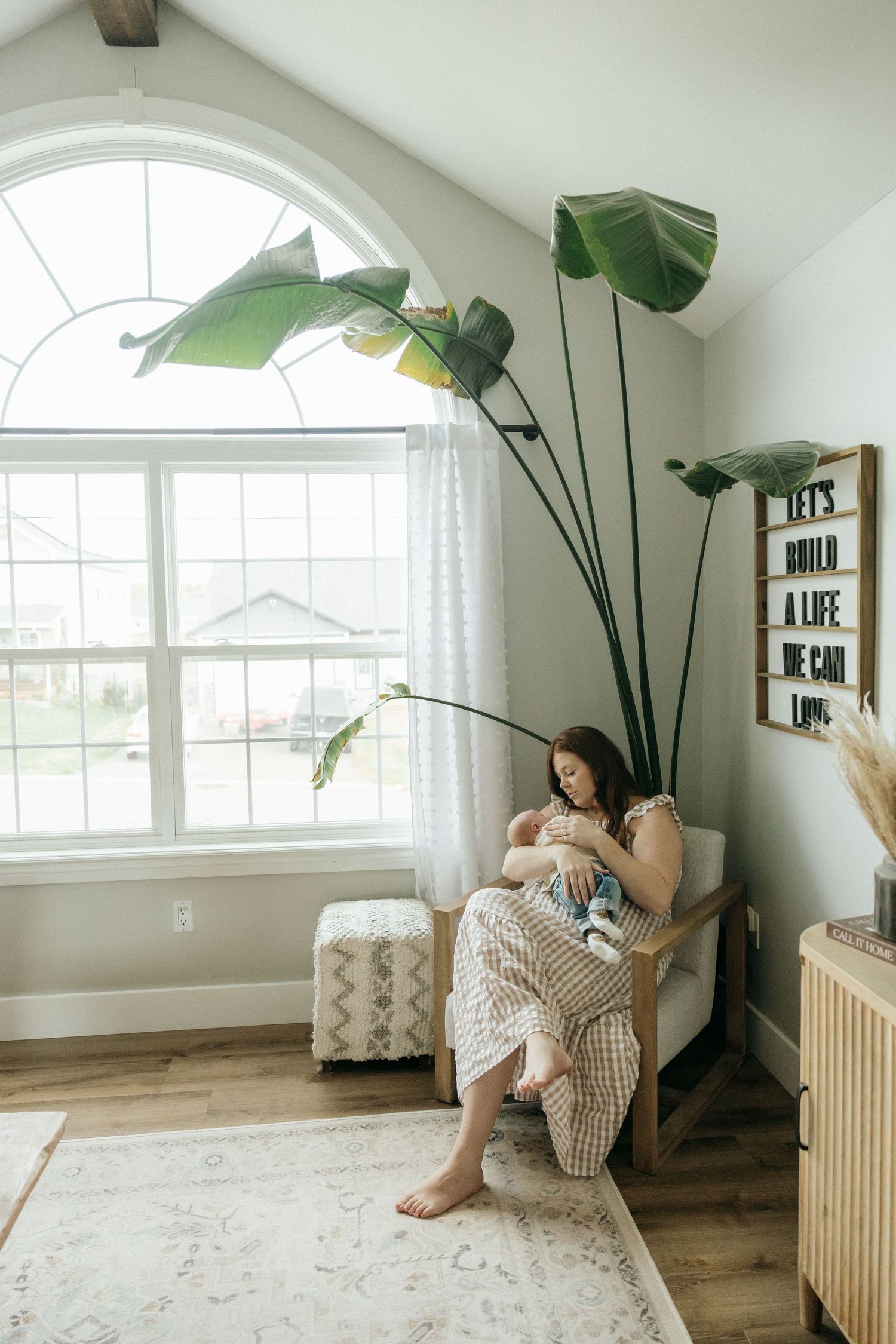 A bright modern living room with large windows, plants, and natural wood accents.