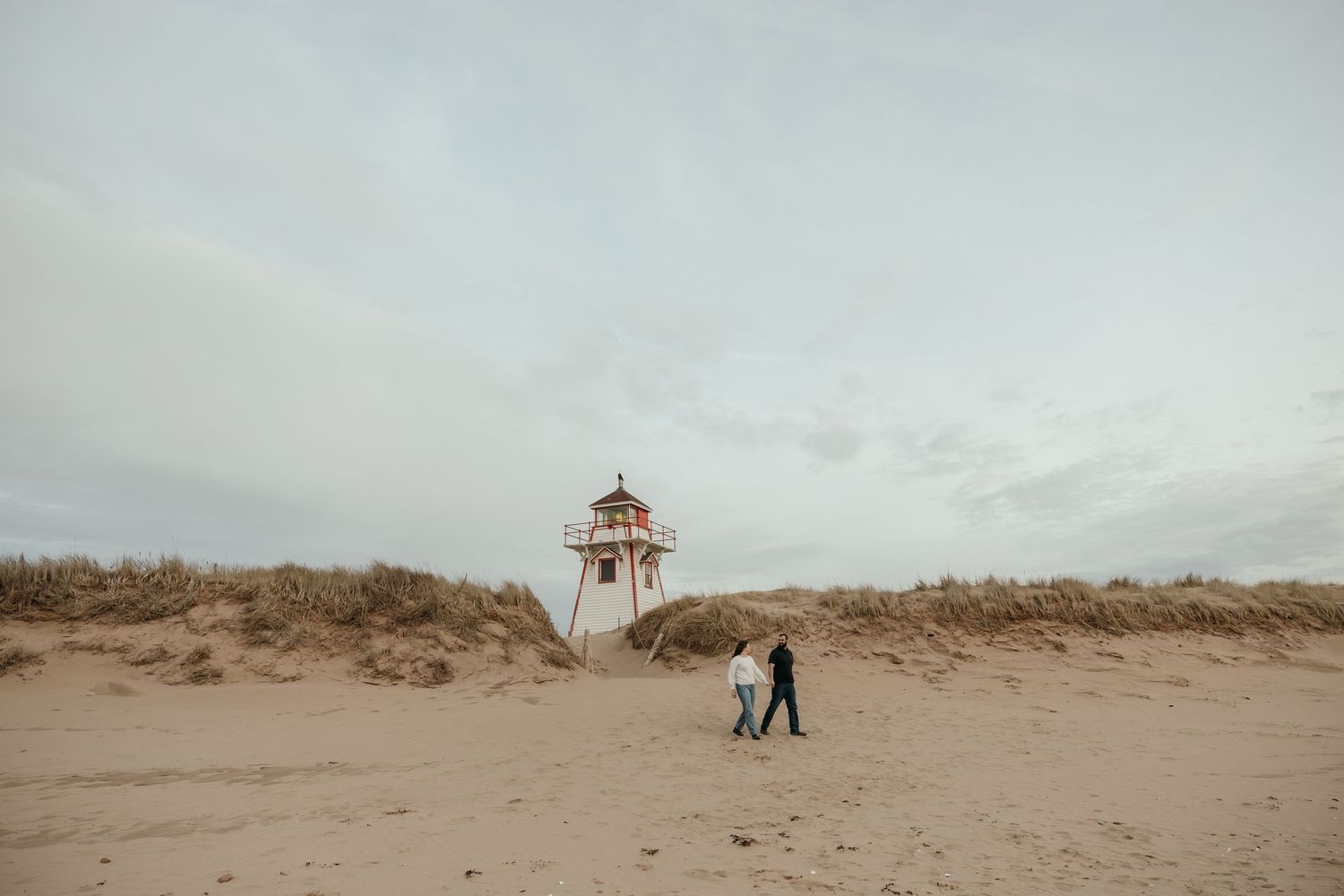 Silhouettes of people walking on a sandy beach near a lifeguard tower at dusk.