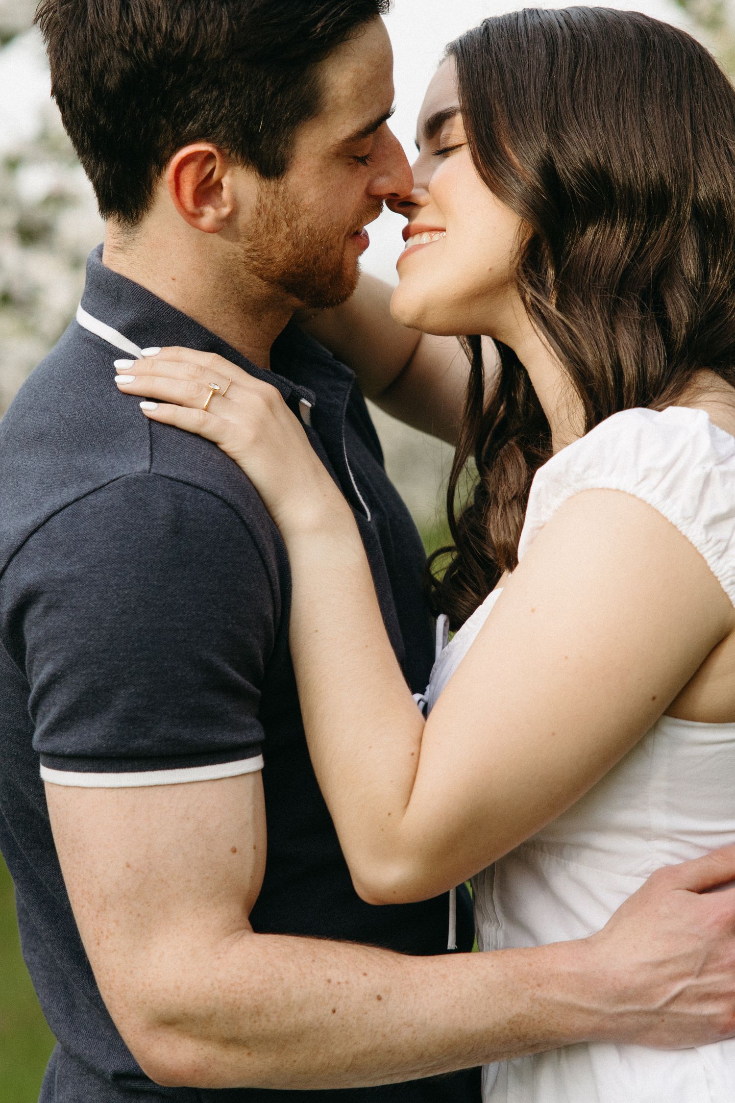 Romantic couple sharing a tender moment, nearly kissing outdoors among spring blossoms.