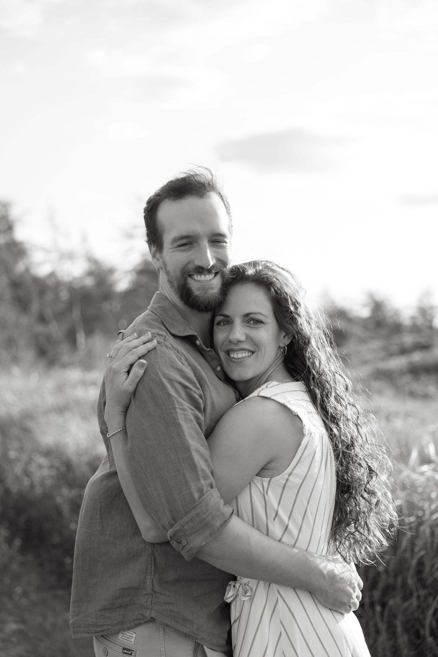 Black and white portrait of a smiling couple embracing outdoors in a field.