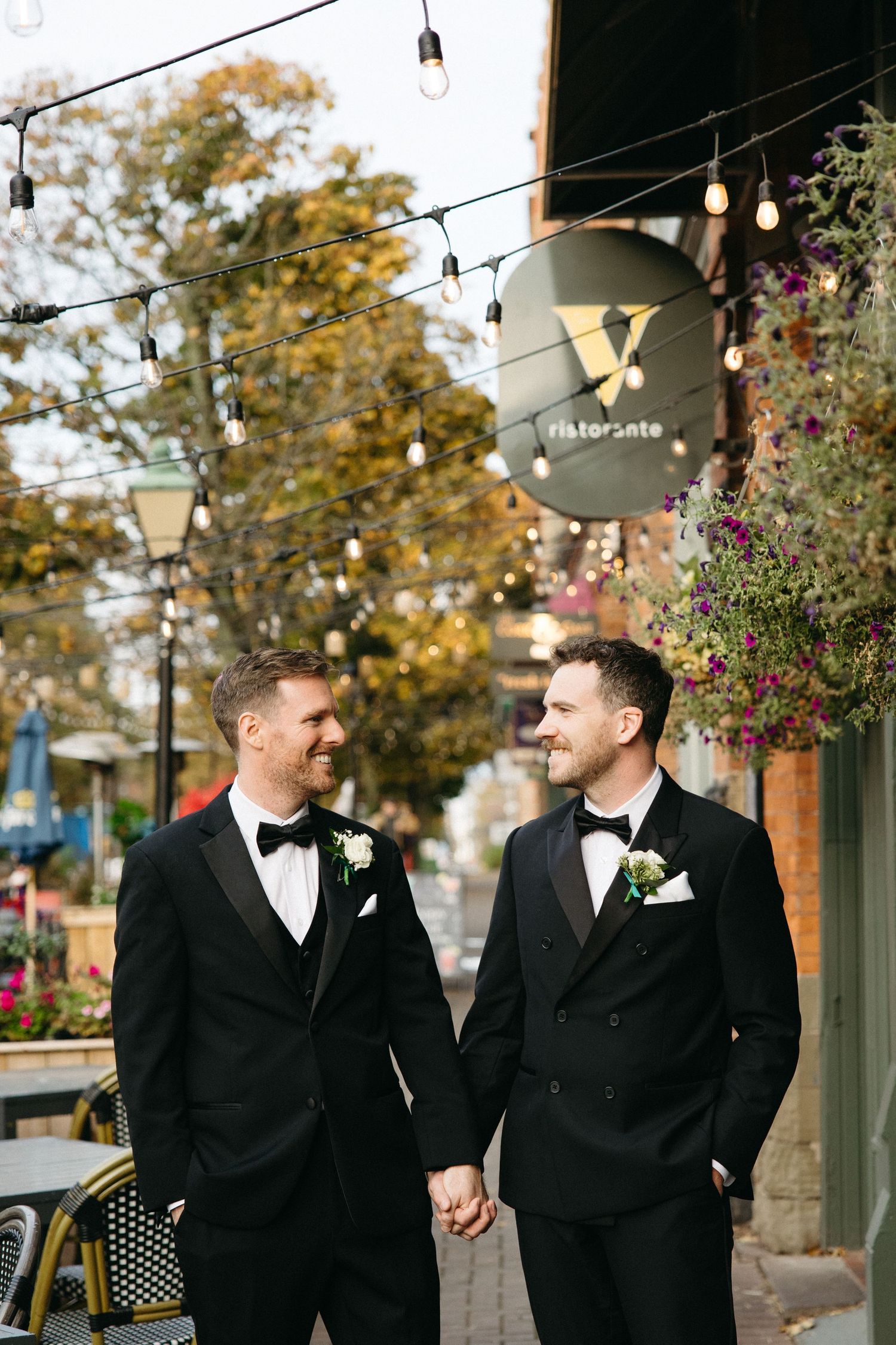 Groomsmen walking together outdoors with string lights and autumn foliage in background.