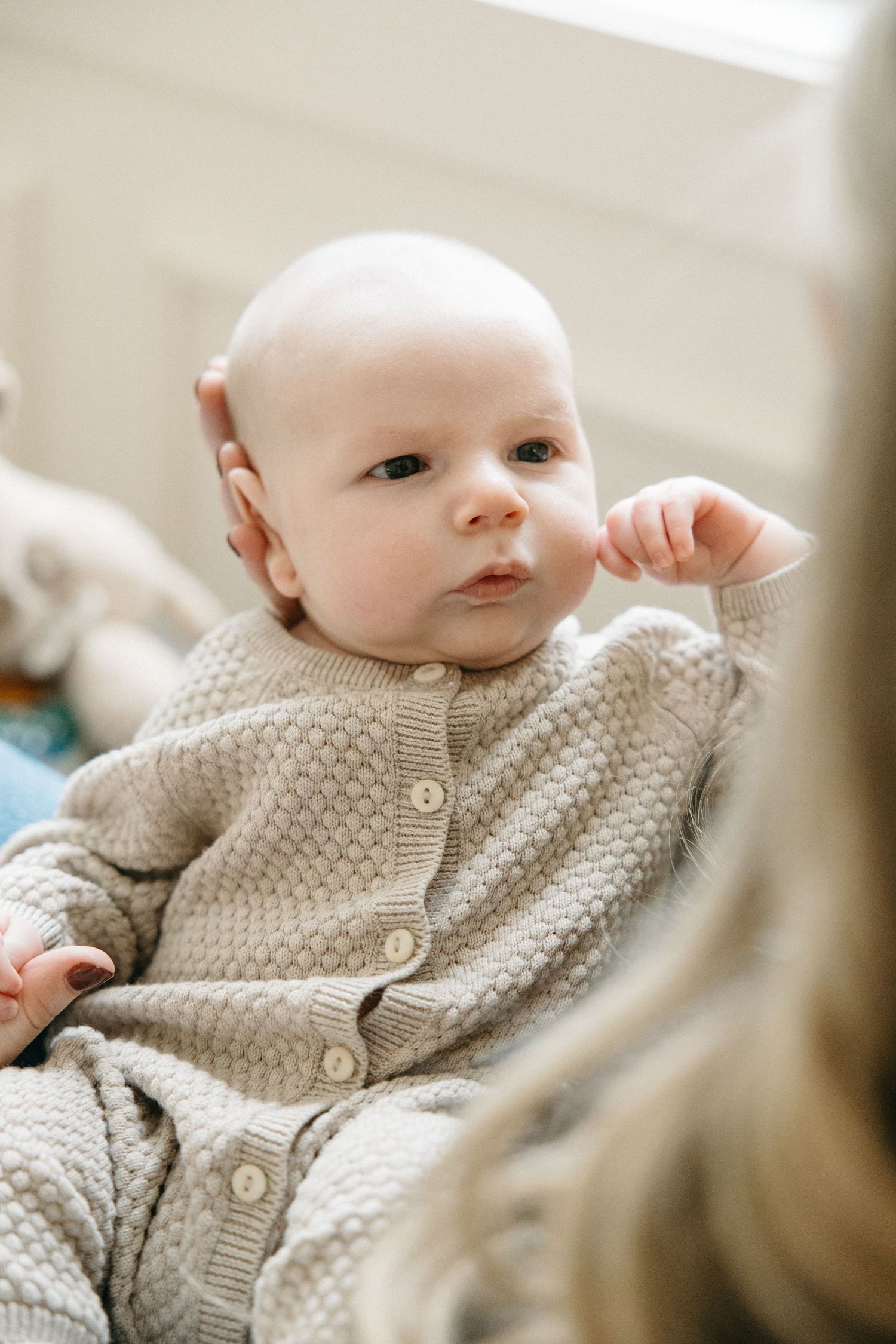 Baby wearing a beige knit cardigan sweater lying down and looking up.