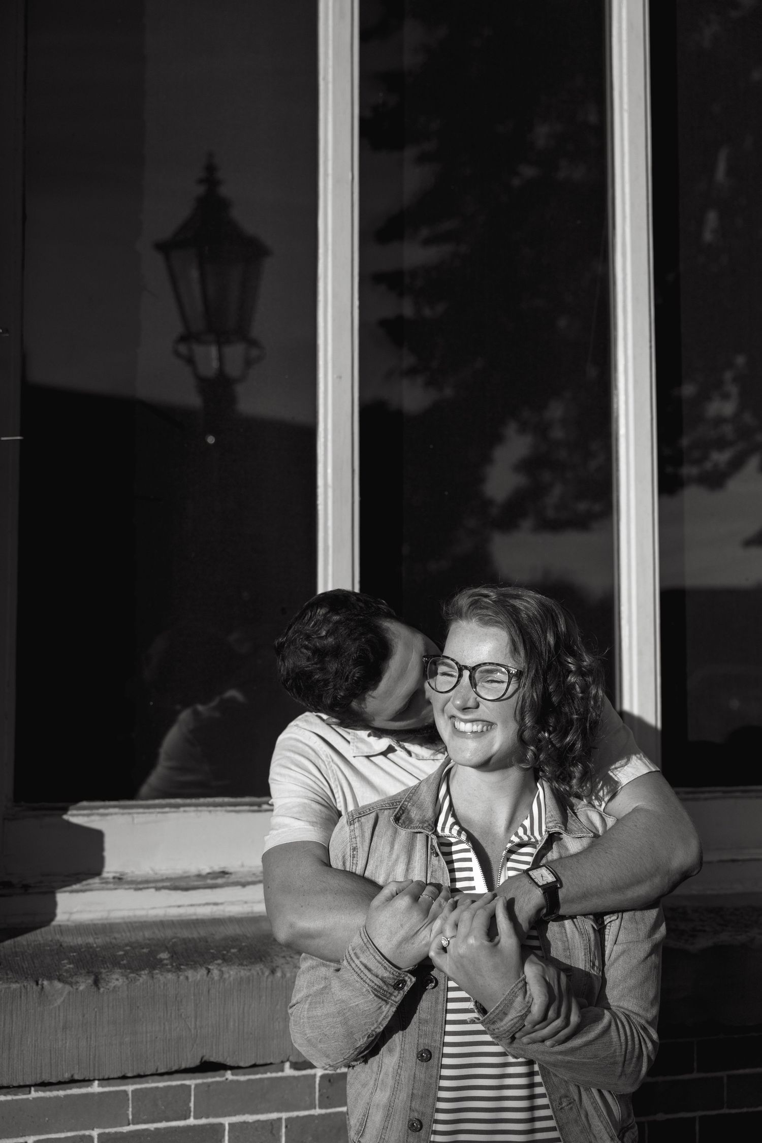 A couple shares a joyful moment together while sitting on a bench in black and white.