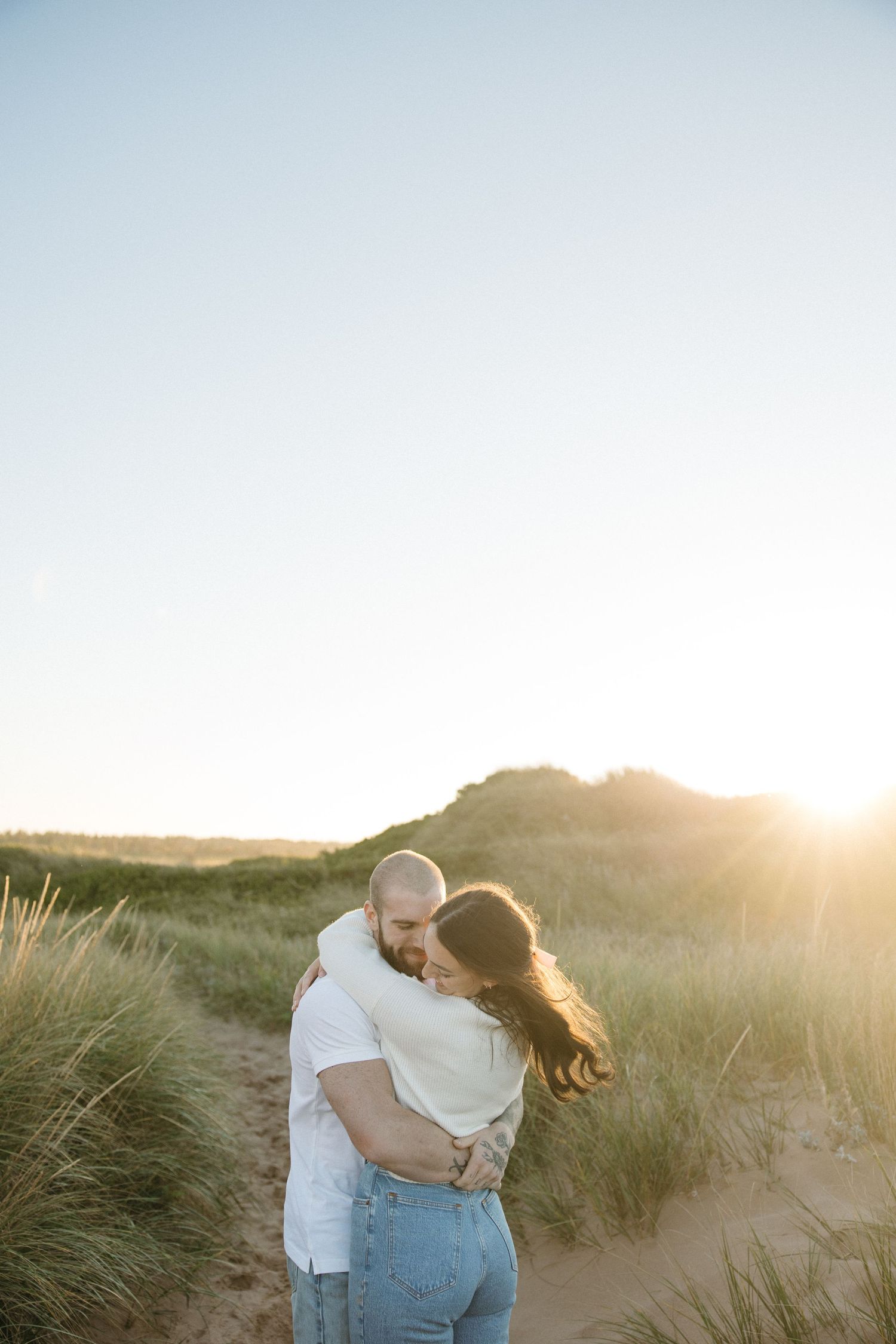 Couple sharing romantic embrace on sandy dunes during sunset.