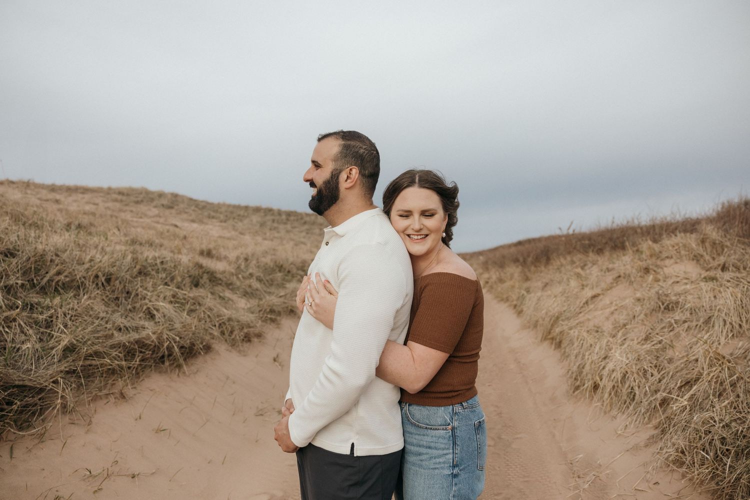 Candid photos of a couple sharing intimate moments on sandy dunes.