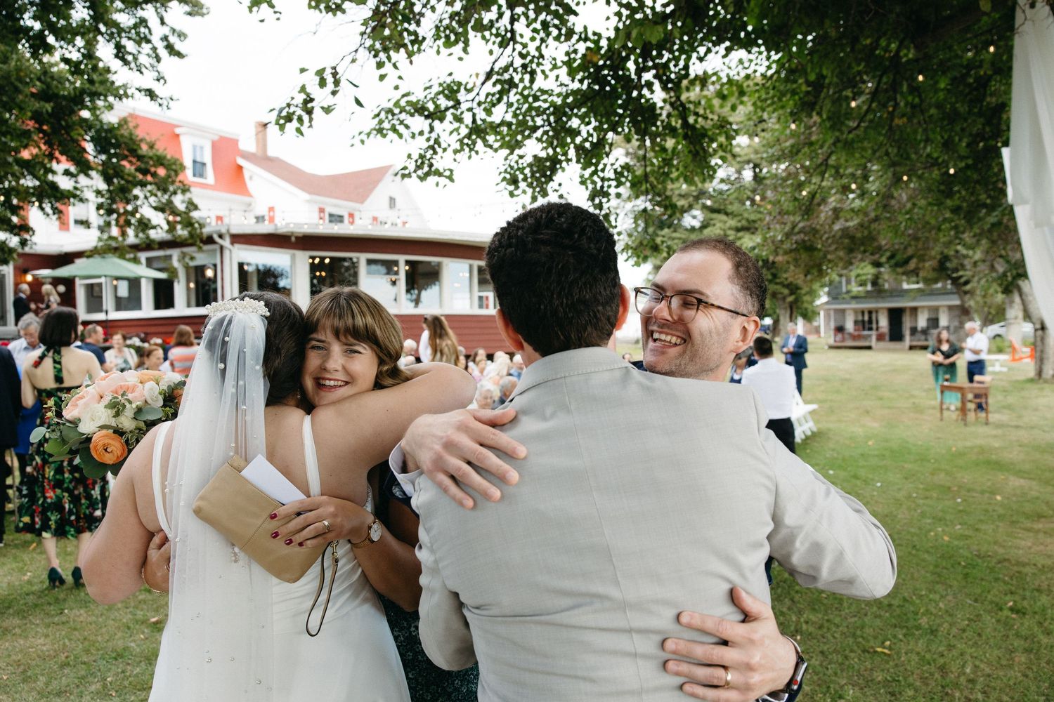 Joyful wedding guests hugging newlyweds outdoors after ceremony on lawn.