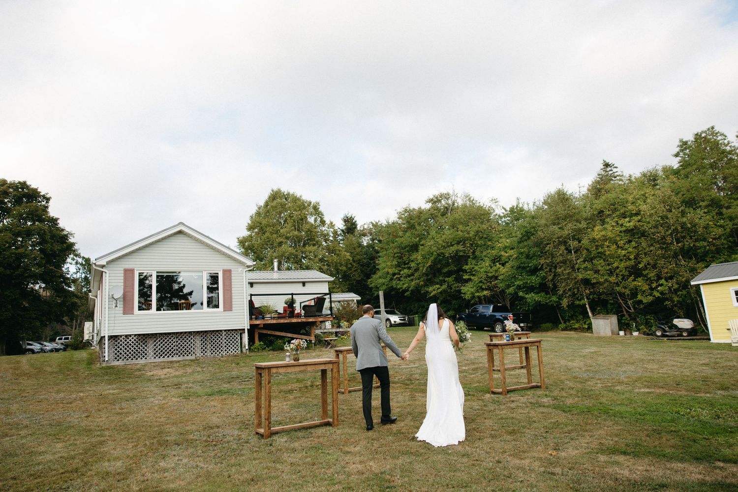 Panoramic view of an outdoor wedding setup with wooden benches and white decor.
