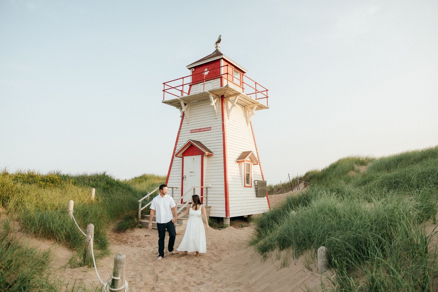 Scenic view of a red and white lighthouse on sand dunes against a bright sky.