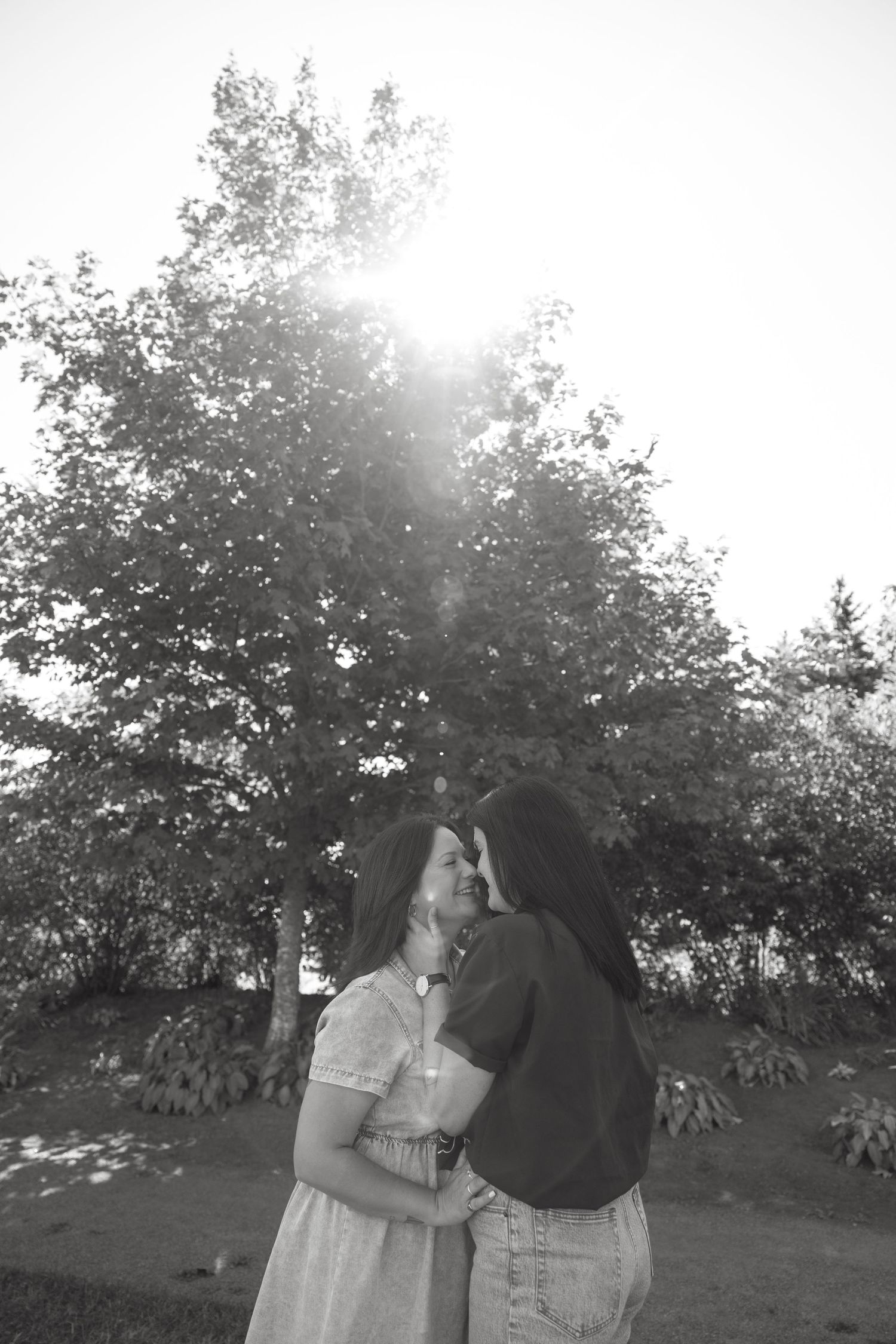 Black and white portrait of a couple in a romantic outdoor setting with sunlit trees.
