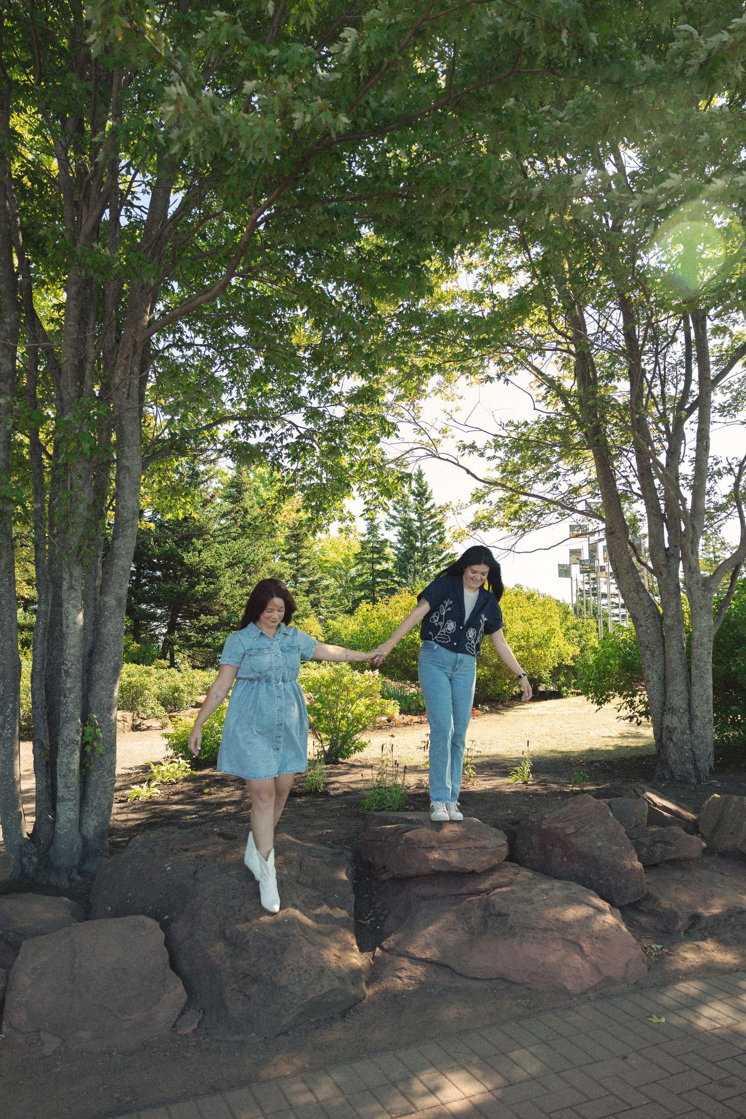 Two people walking on large rocks surrounded by trees in a scenic park setting.