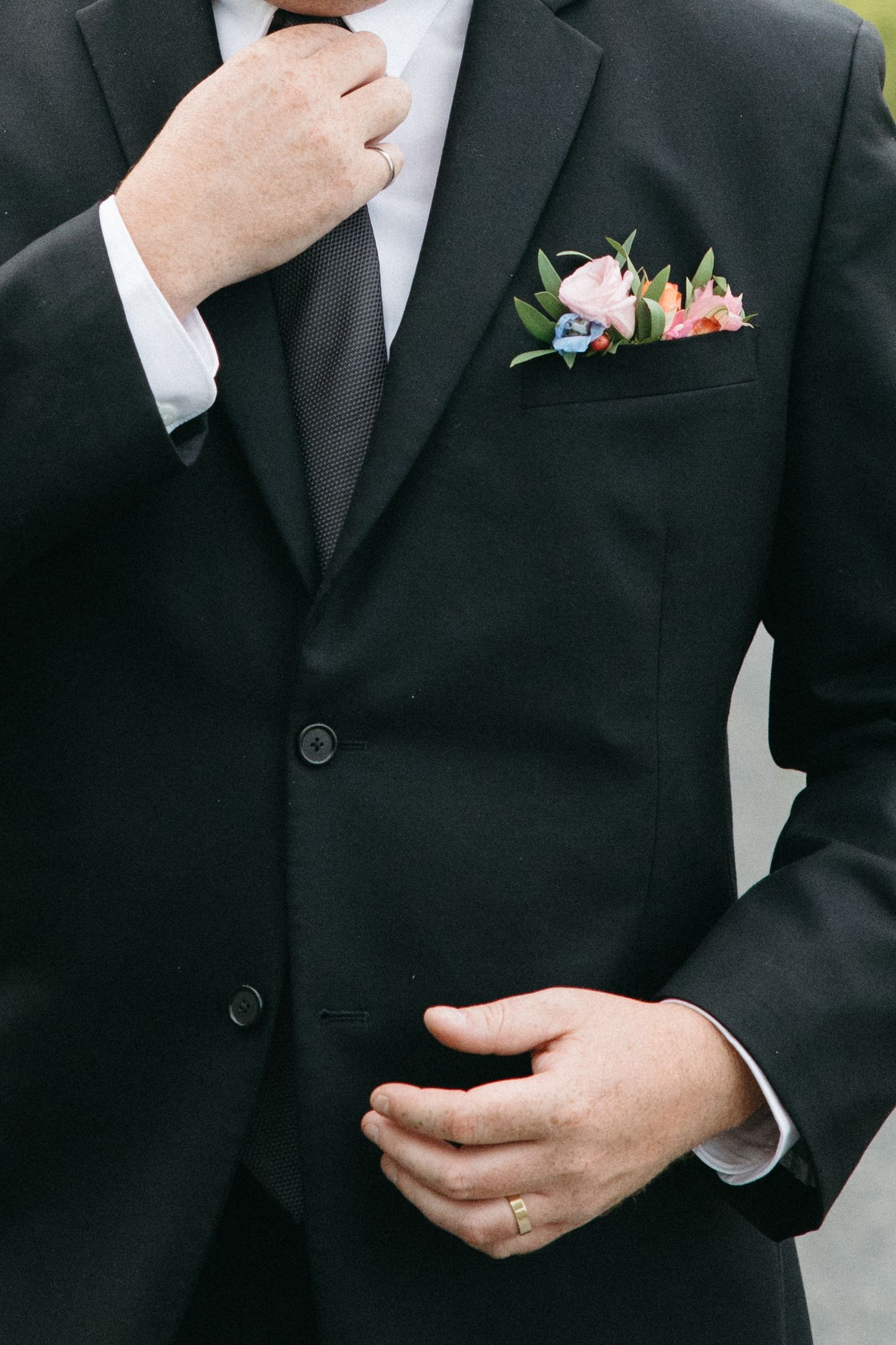 Close-up details of black suit jacket with pink floral boutonniere.