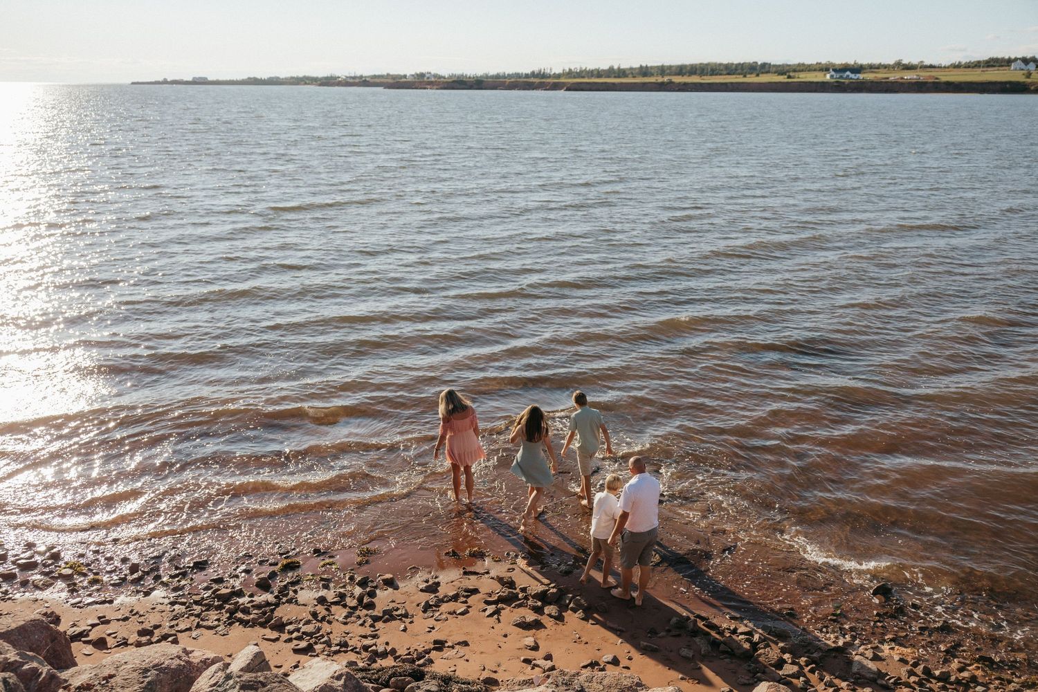 Family playing together at the water's edge during golden hour.