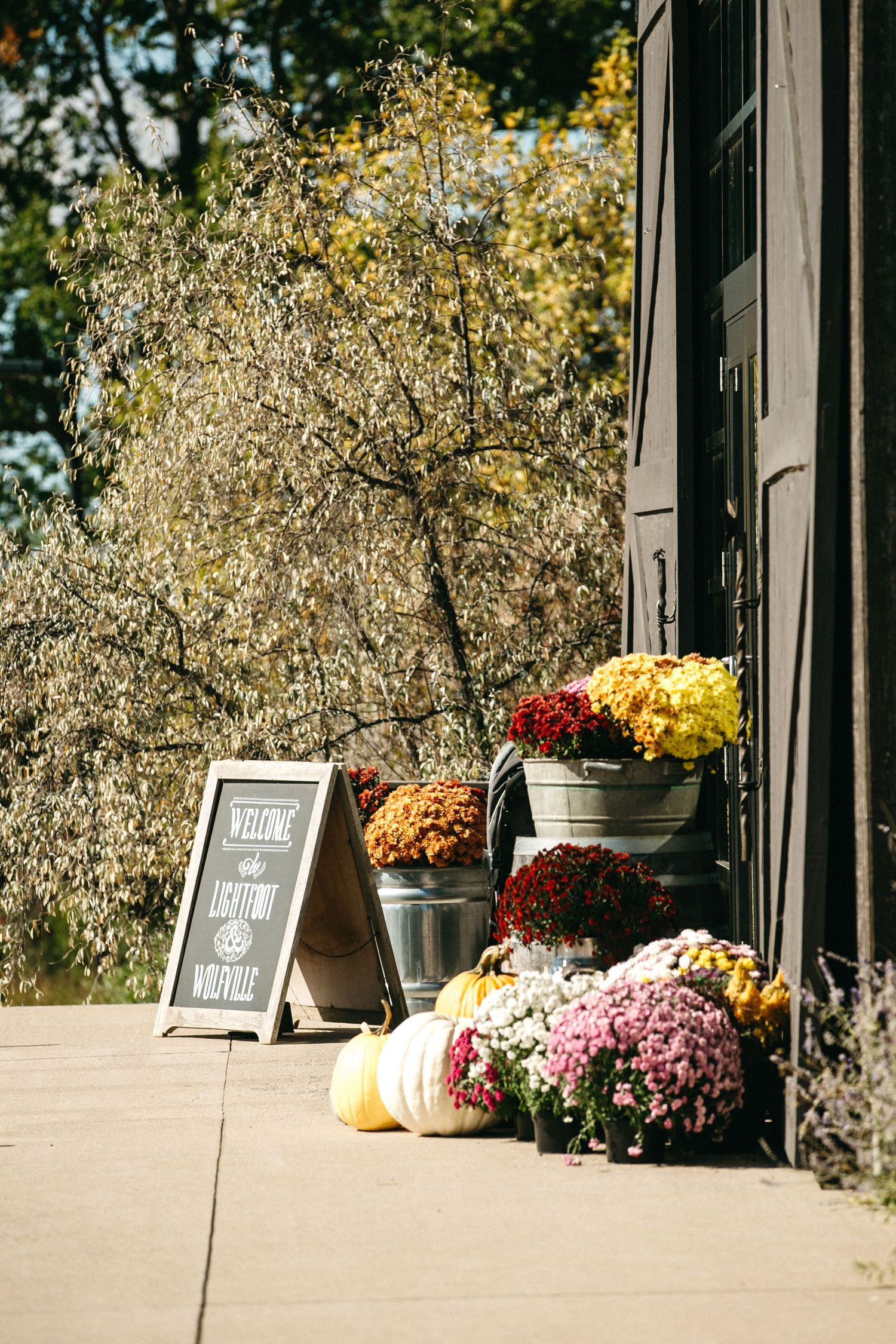 Fall decorations and colorful mums adorn a rustic outdoor porch with chalkboard signs.