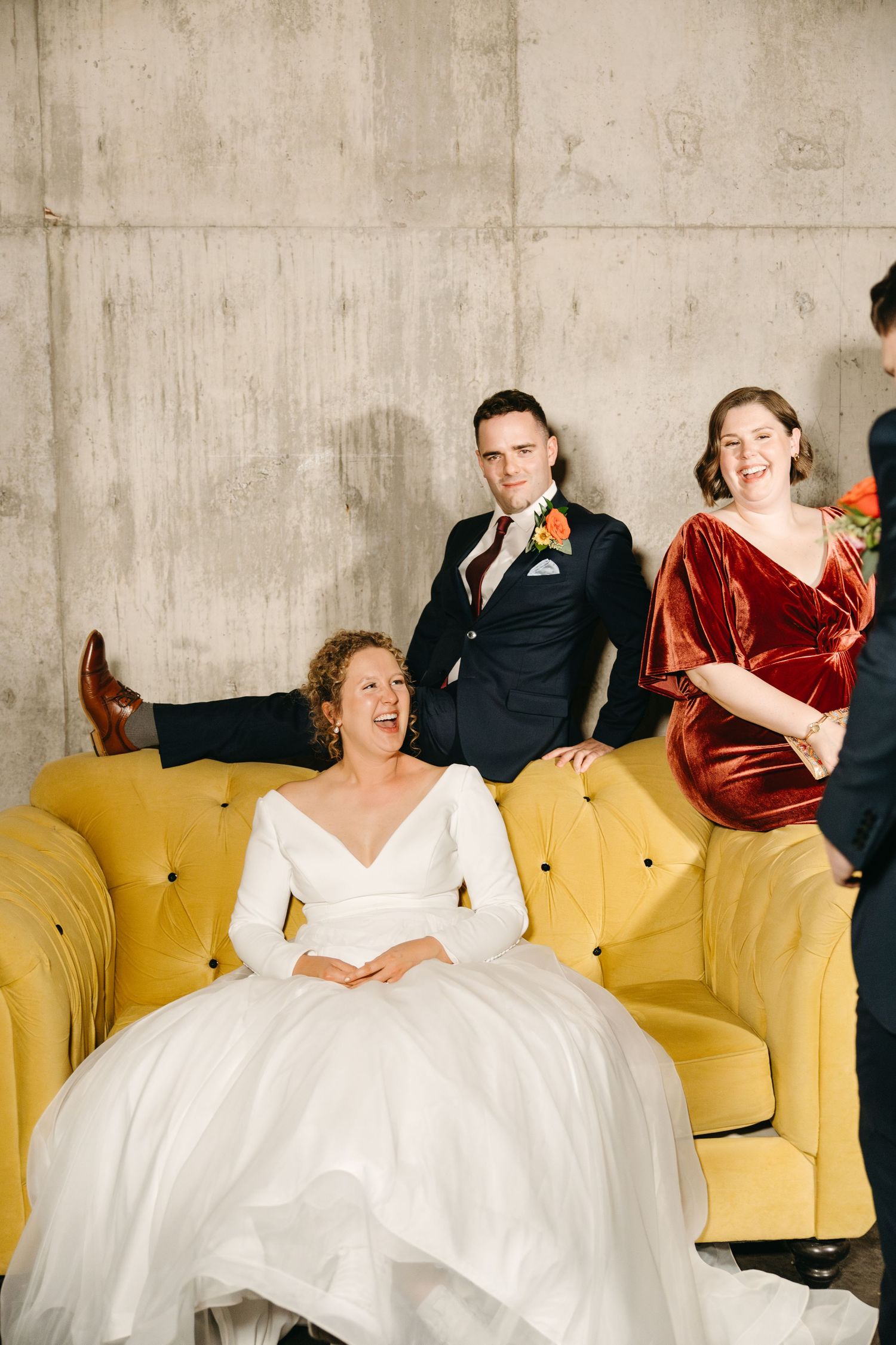 Candid moments of wedding party lounging on yellow couch in modern industrial setting.