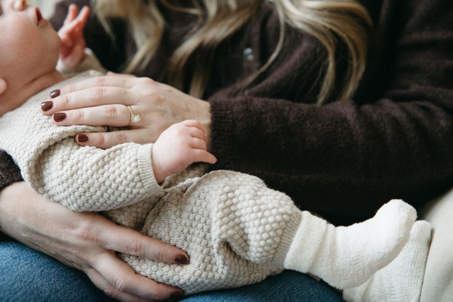 Close-up of hands cradling a sleeping newborn in cream knit blanket.