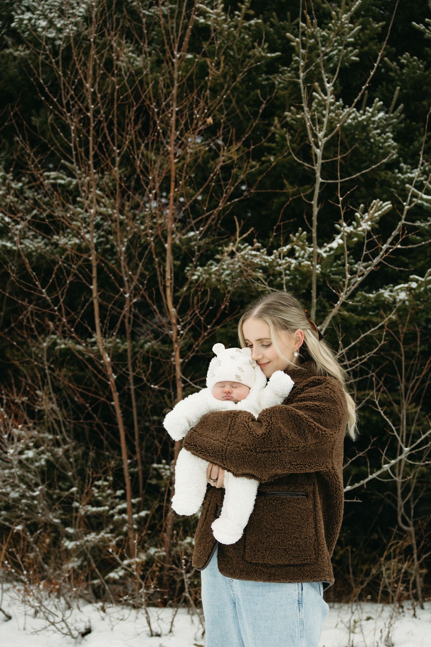 Winter family photoshoot in snow with baby wearing white outfit.
